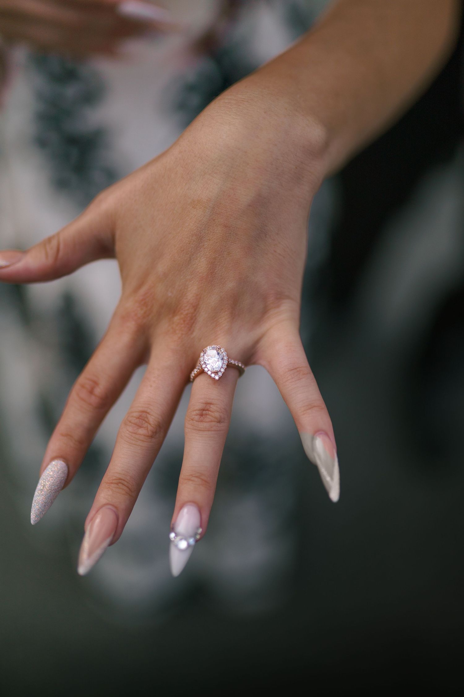 Close-up shots of a hand wearing a sparkling engagement ring with white manicured nails against a blurred background.