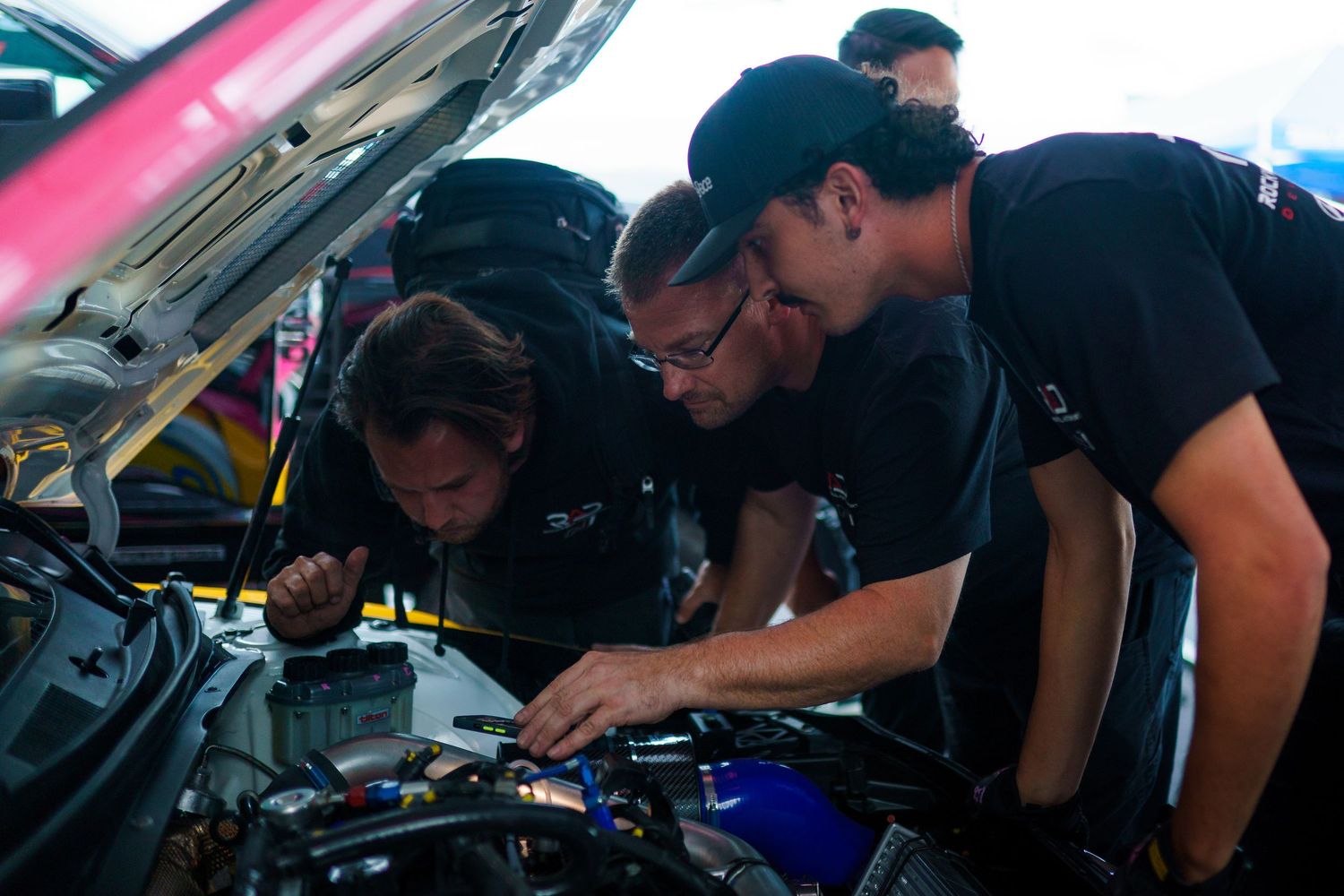 Mechanics working together to inspect and repair a car engine during maintenance service.