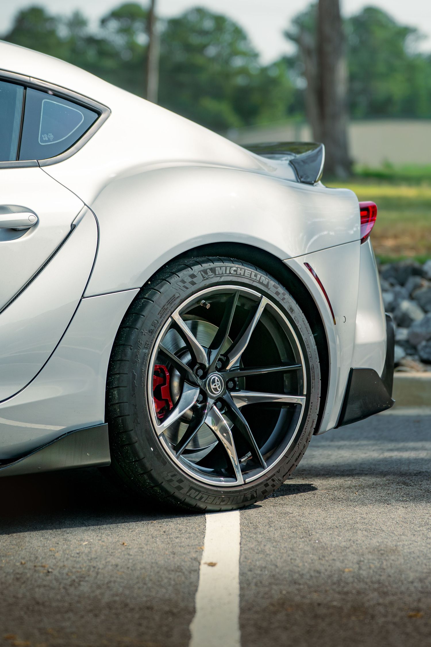 Close-up view of custom white sports car alloy wheels with red brake calipers against an asphalt background.