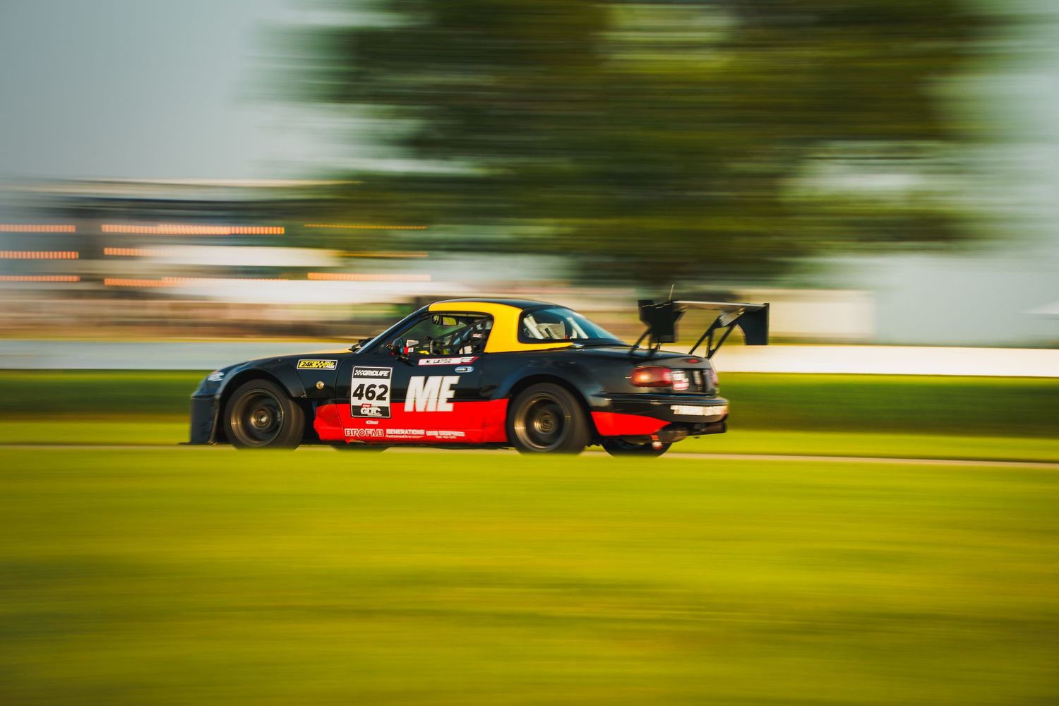 Blurred motion shot of a black race car with red trim speeding around a racetrack at high speed.