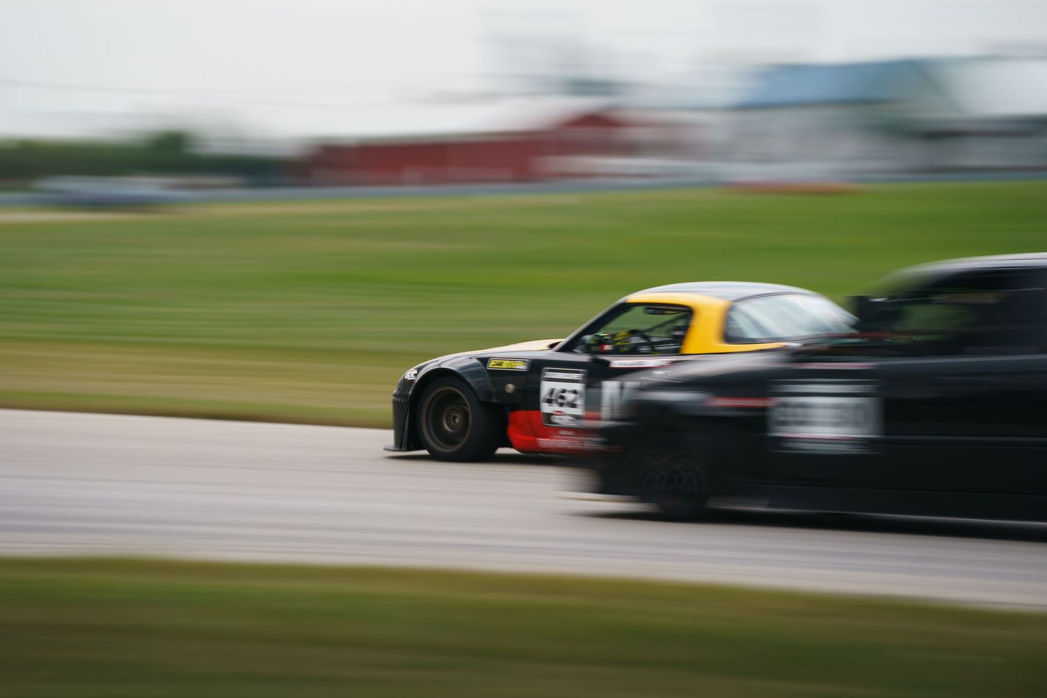 A series of blurred racing cars speeding past on a racetrack during a motorsport competition.