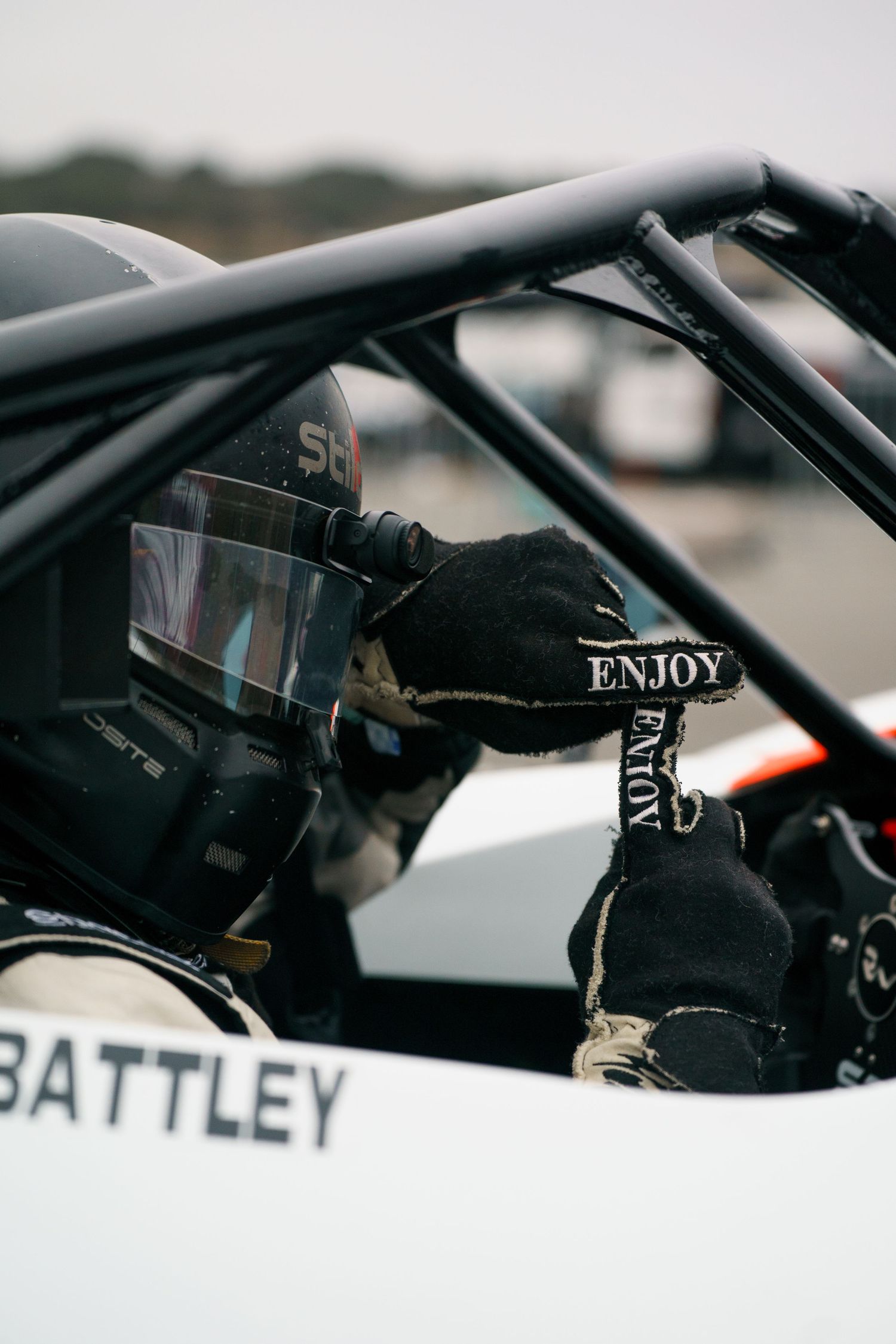 Racing driver wearing black gloves grips steering wheel in cockpit during competitive motorsport event.
