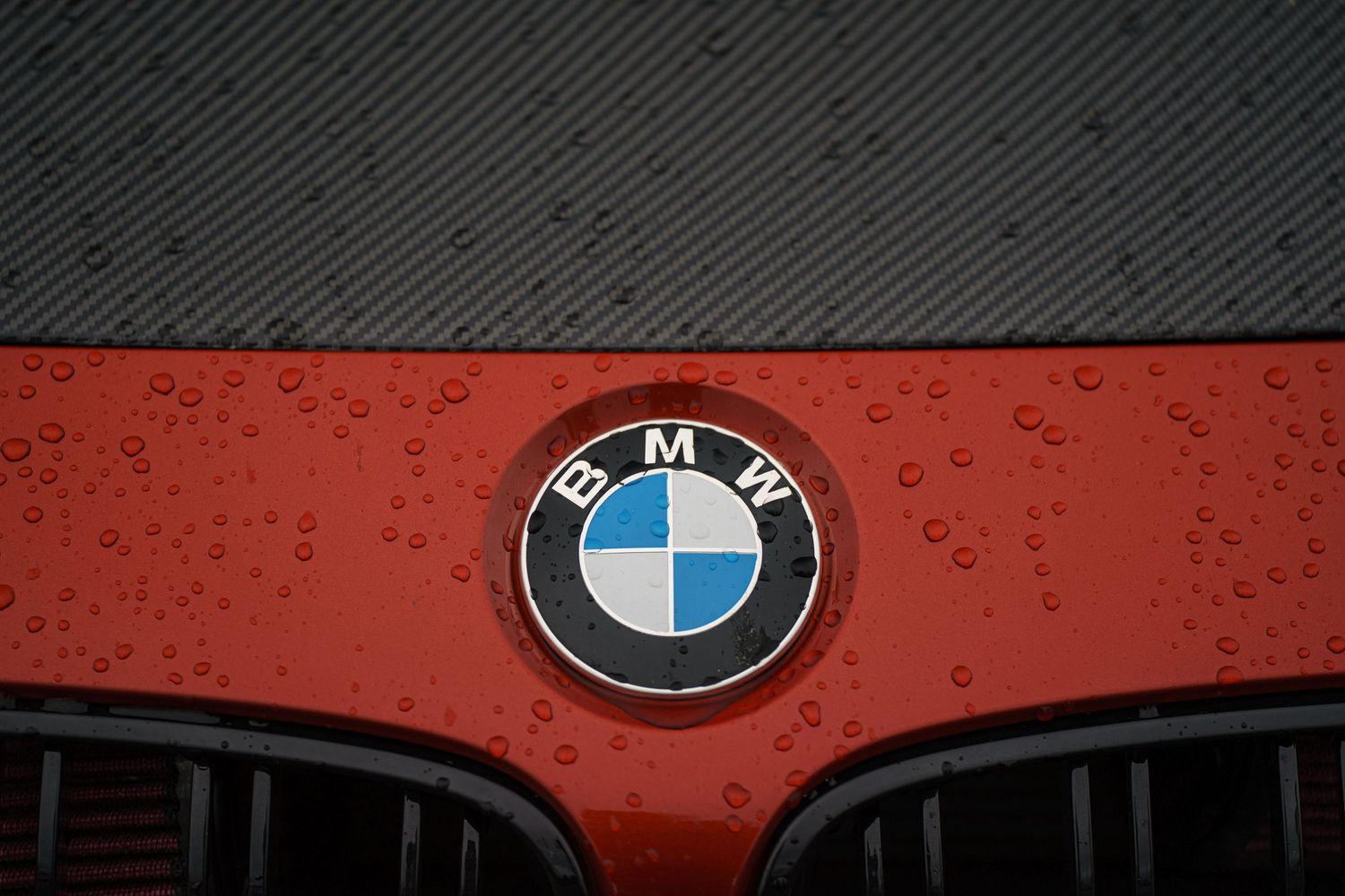 Close-up of BMW badge and logo on red vehicle surface.