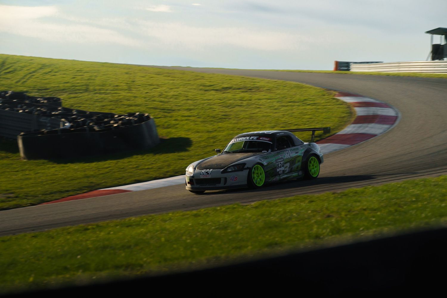 A modified sports car races around a curved track with green grass and barriers in the background.