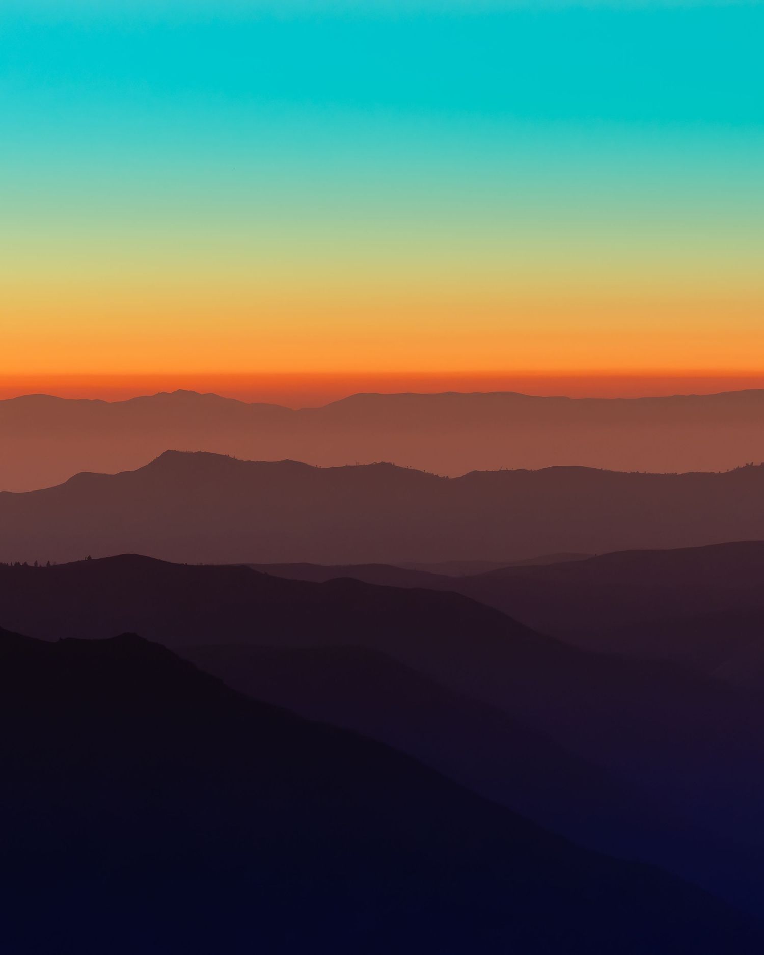 Stunning layered mountain silhouettes at sunset with vibrant gradient sky transitioning from teal to orange over misty ridges.