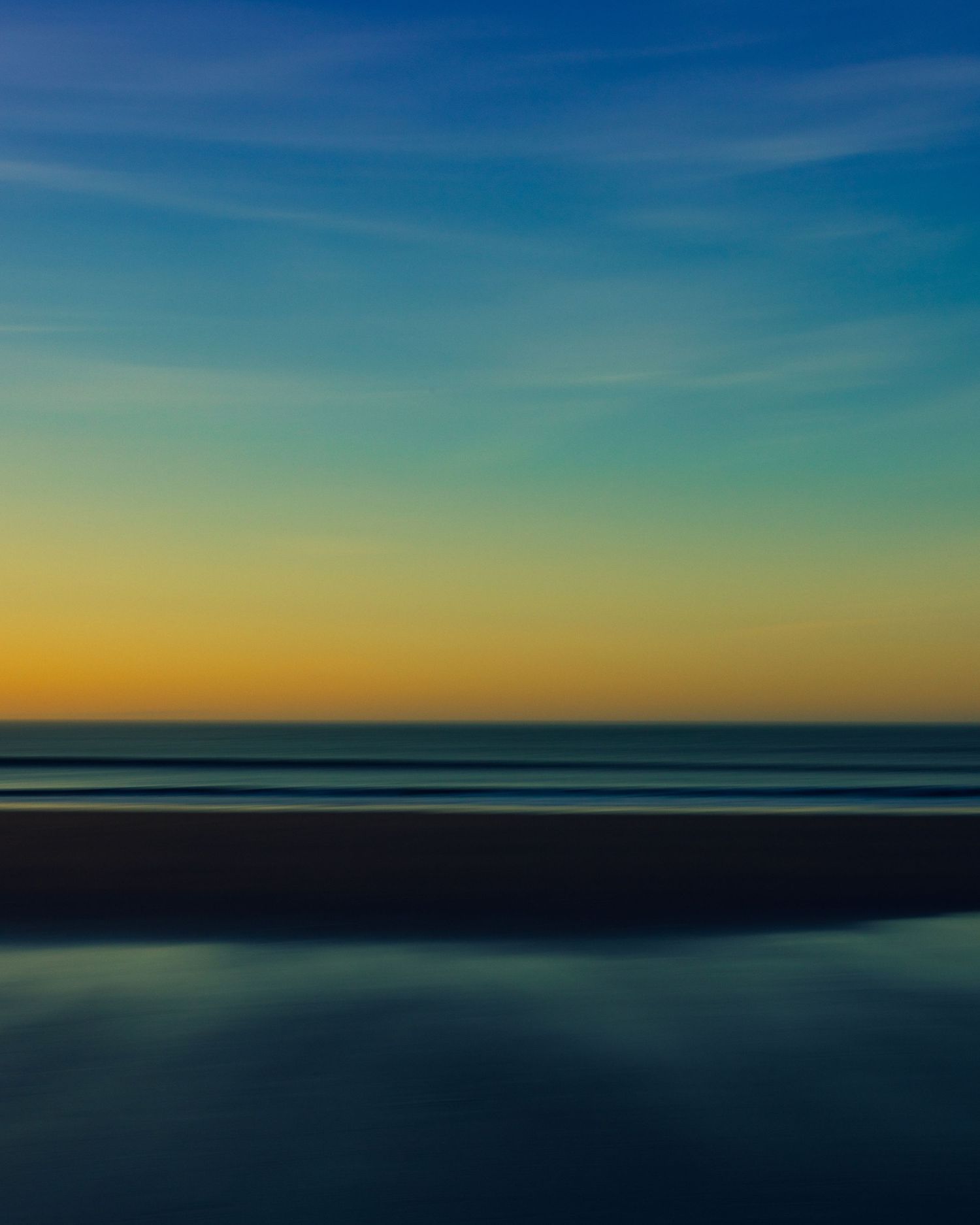A serene beach sunset with golden horizon, calm ocean waters, and a gradient blue sky with wispy clouds.