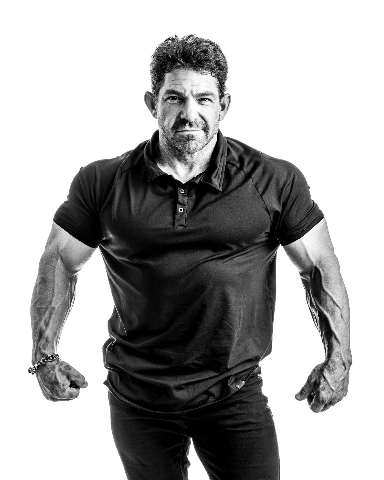 Black and white portrait of a muscular man in a black polo shirt posing with clenched fists.