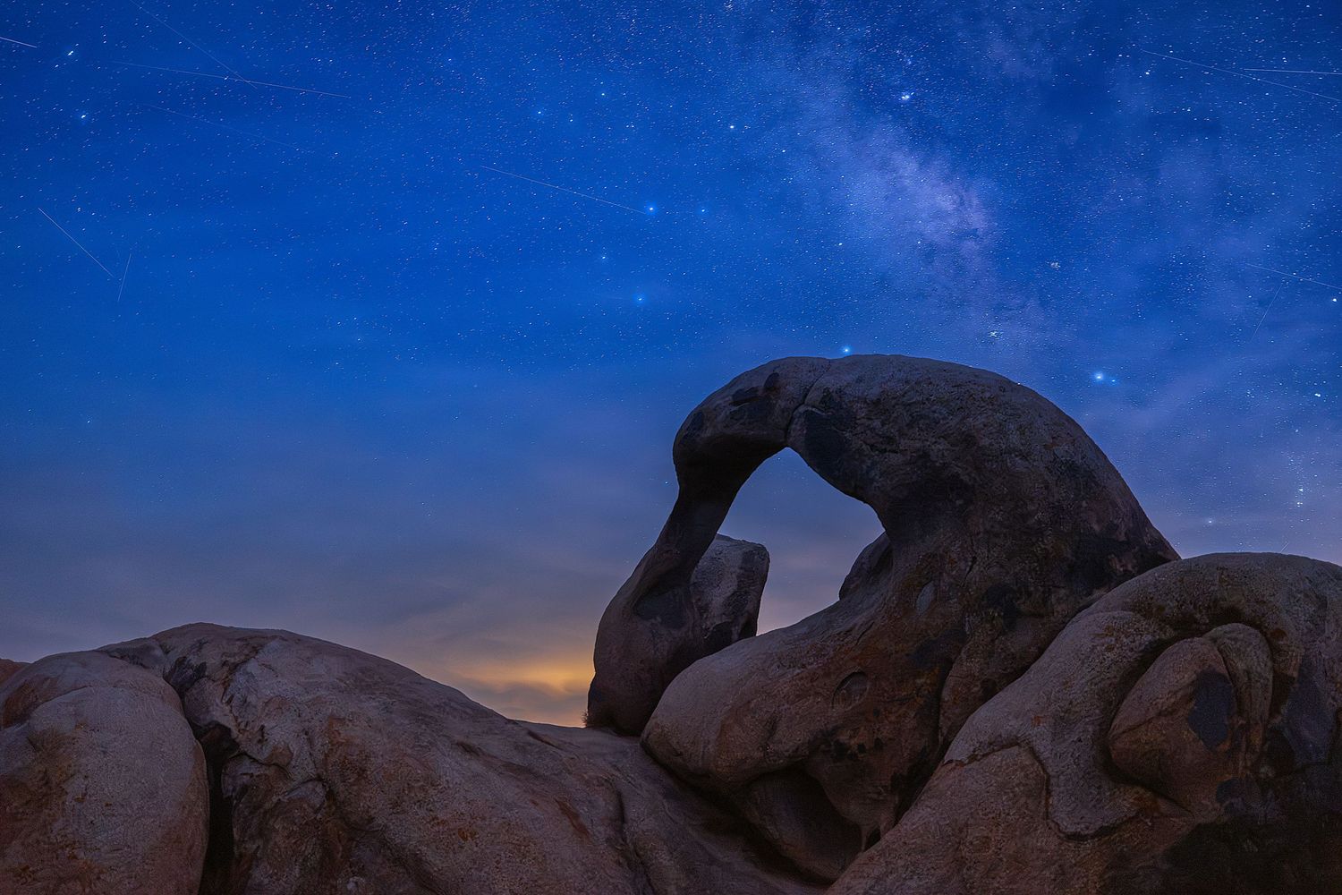 Rocky arch formation silhouetted against a stunning Milky Way night sky in the desert.
