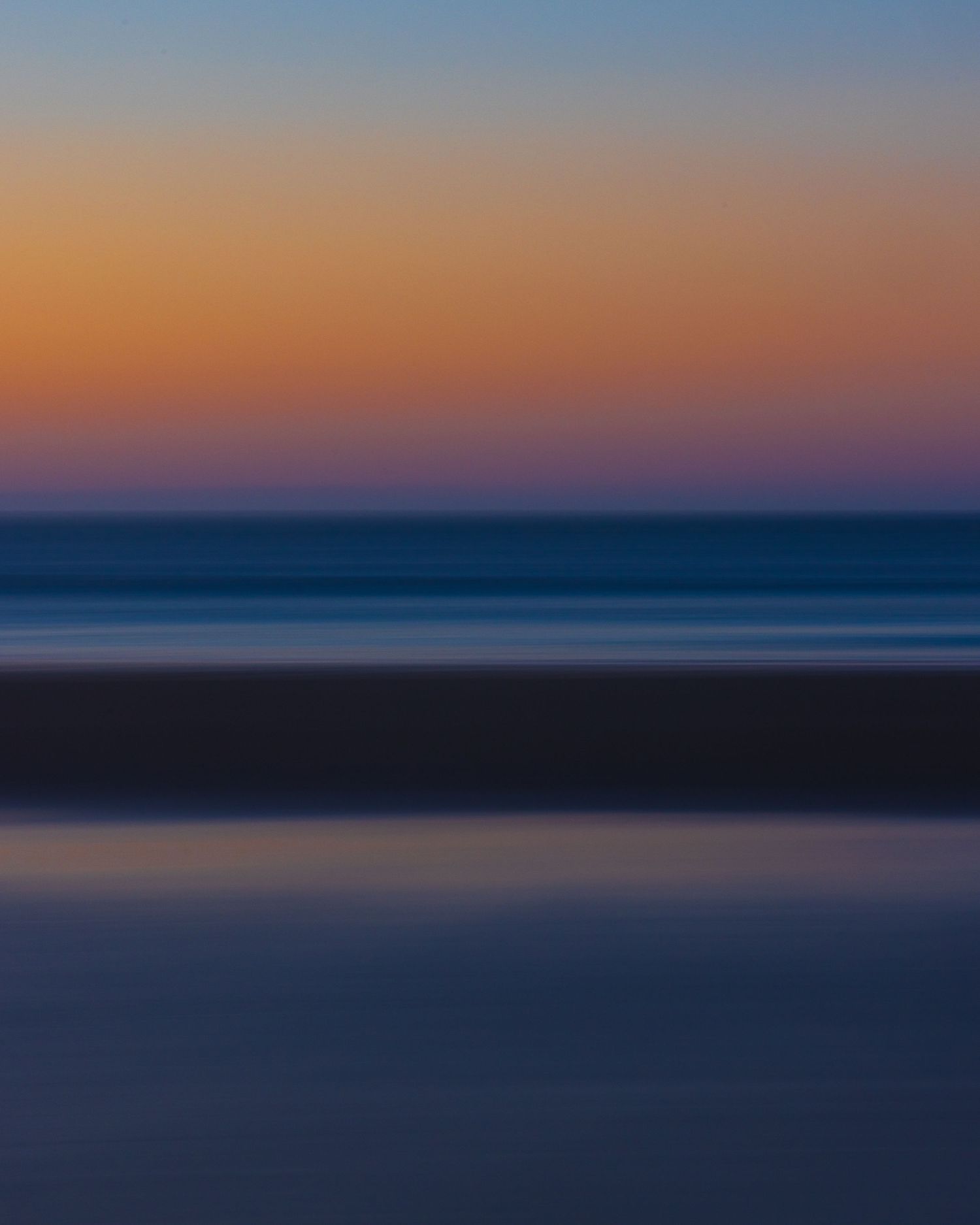 Abstract blurred seascape at sunset with warm orange and pink sky gradient over calm blue ocean.
