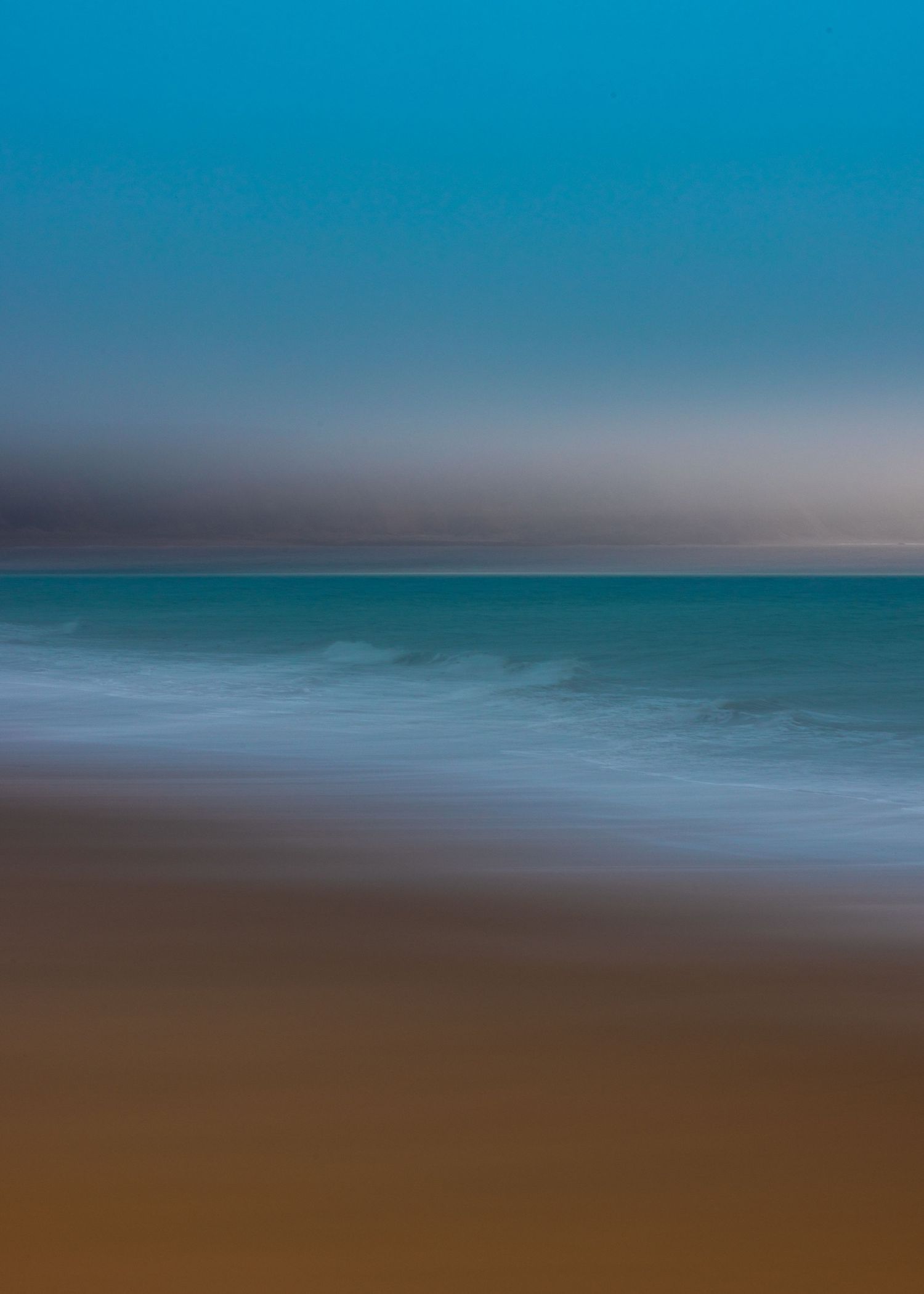 Abstract blurred coastal scene with turquoise sea, white foam waves, and sandy beach at twilight.