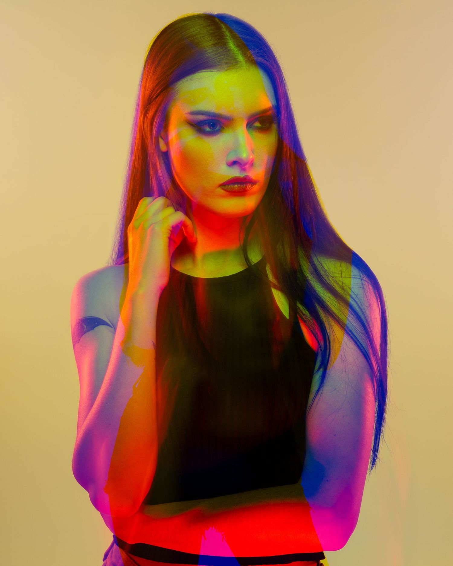 Portrait of a woman with long hair in dramatic multicolored neon lighting against a neutral background.