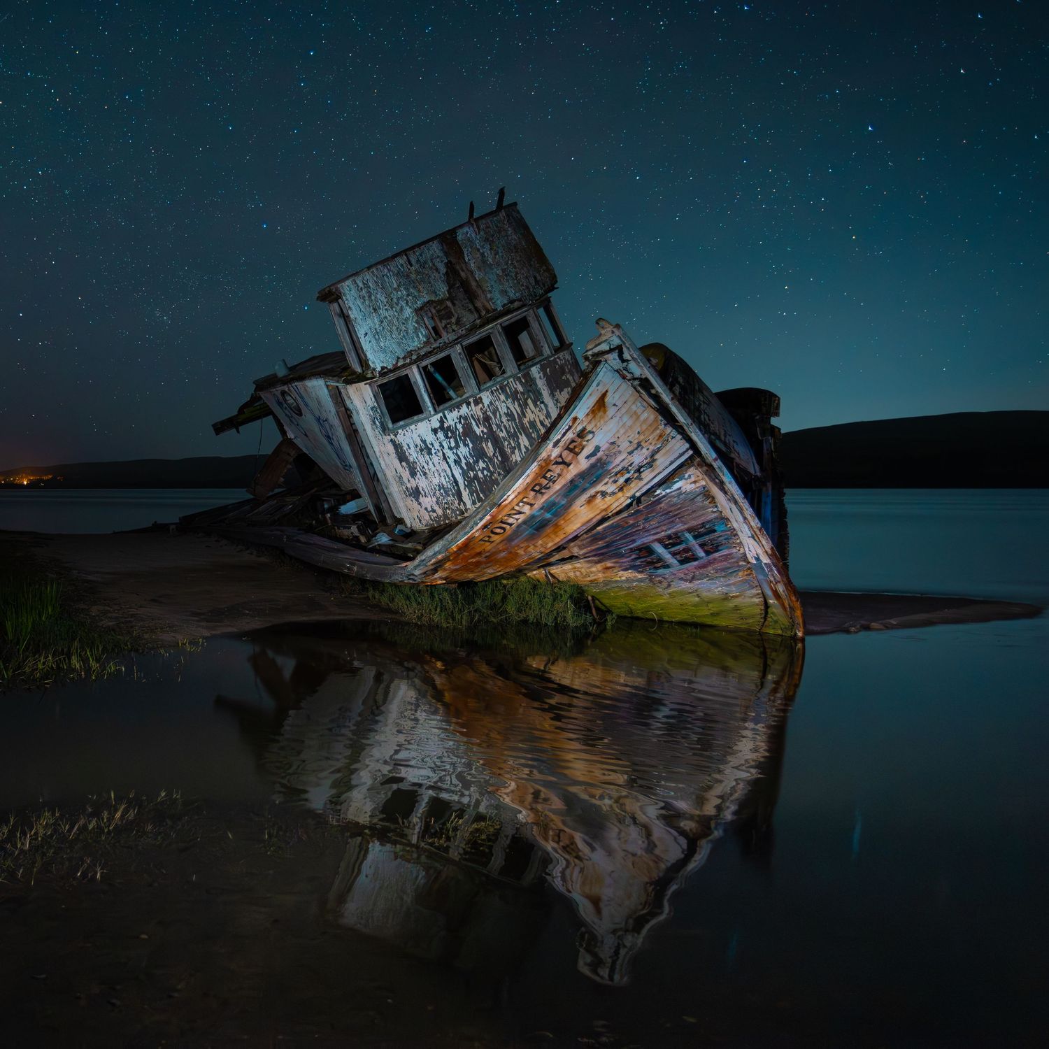 Abandoned shipwreck reflecting in still water under a stunning starry night sky.