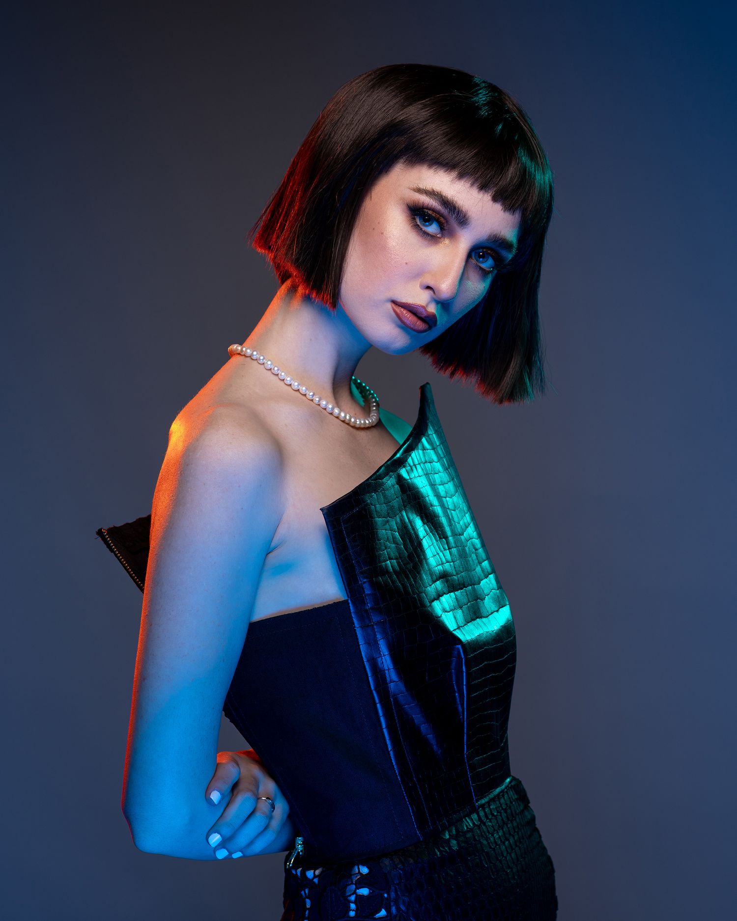 Portrait of a woman with a bob haircut in blue and red neon lighting wearing a pearl necklace.