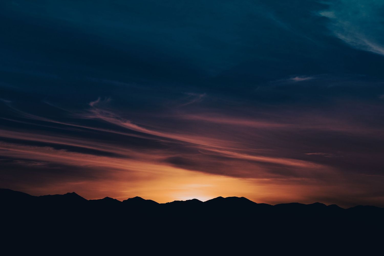 Mountain silhouette at sunset with vivid orange and red streaks across a dark blue sky.