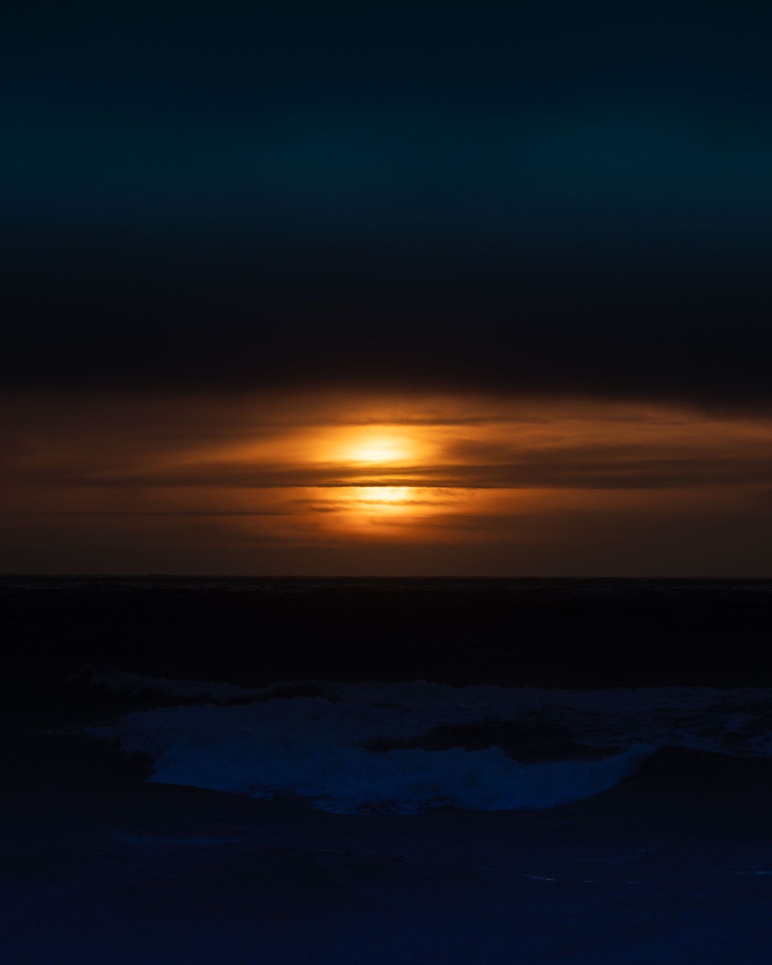 Dark dramatic seascape with glowing orange moon rising through clouds over a dark ocean at night.