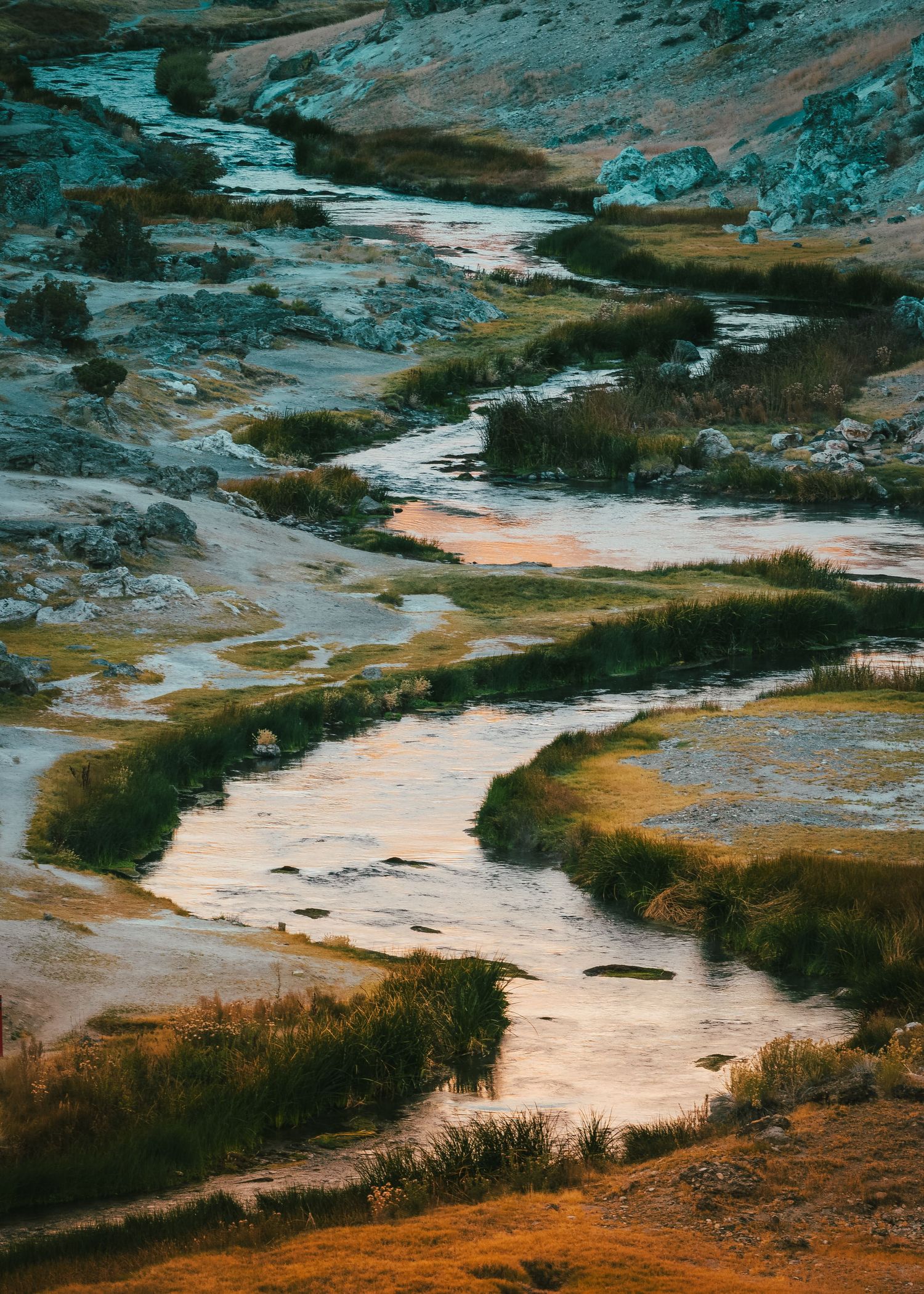 Aerial view of a winding river through colorful mineral-rich terrain in a valley.
