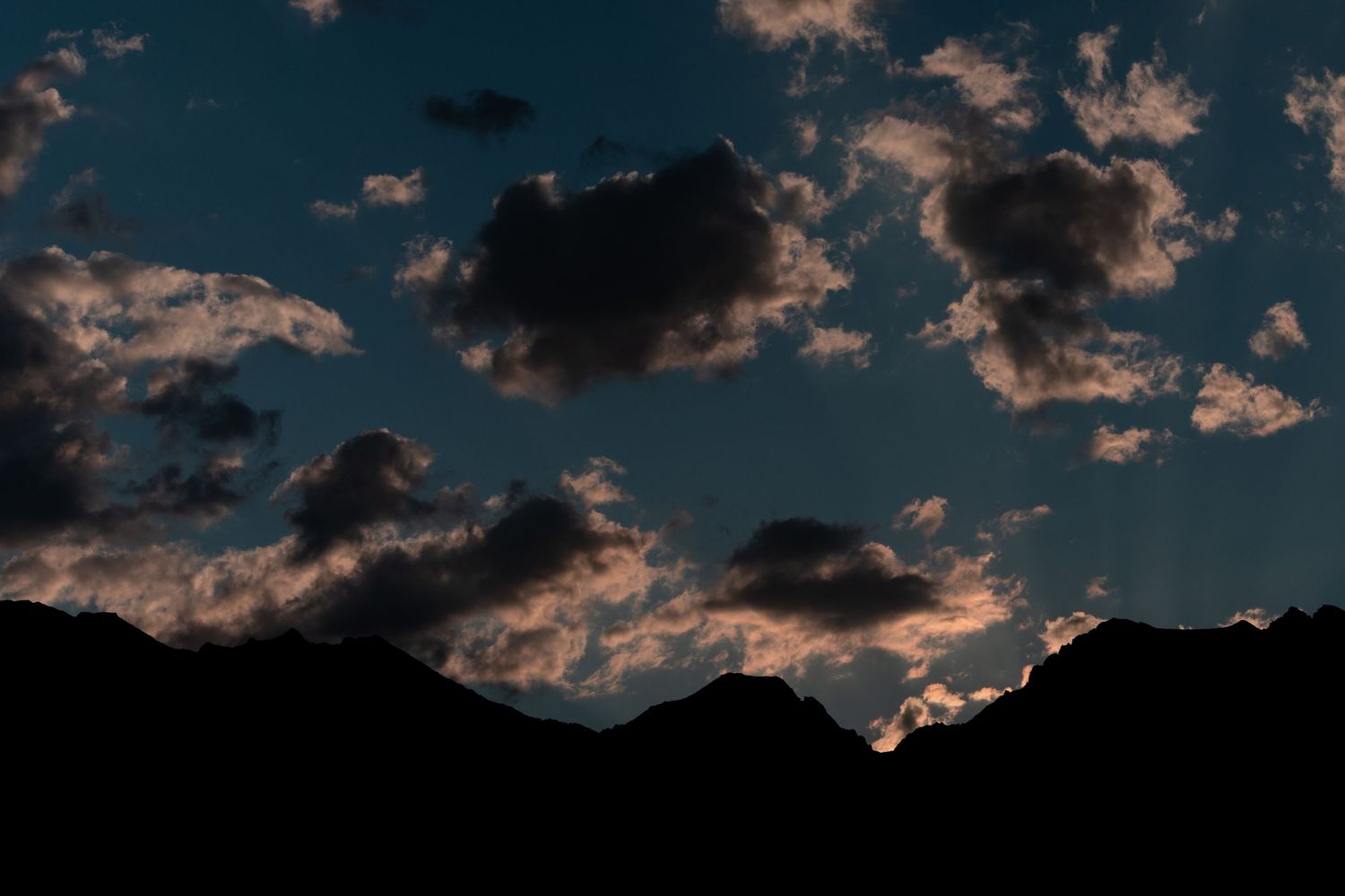 Dramatic twilight sky with glowing clouds over dark mountain silhouettes at dusk.