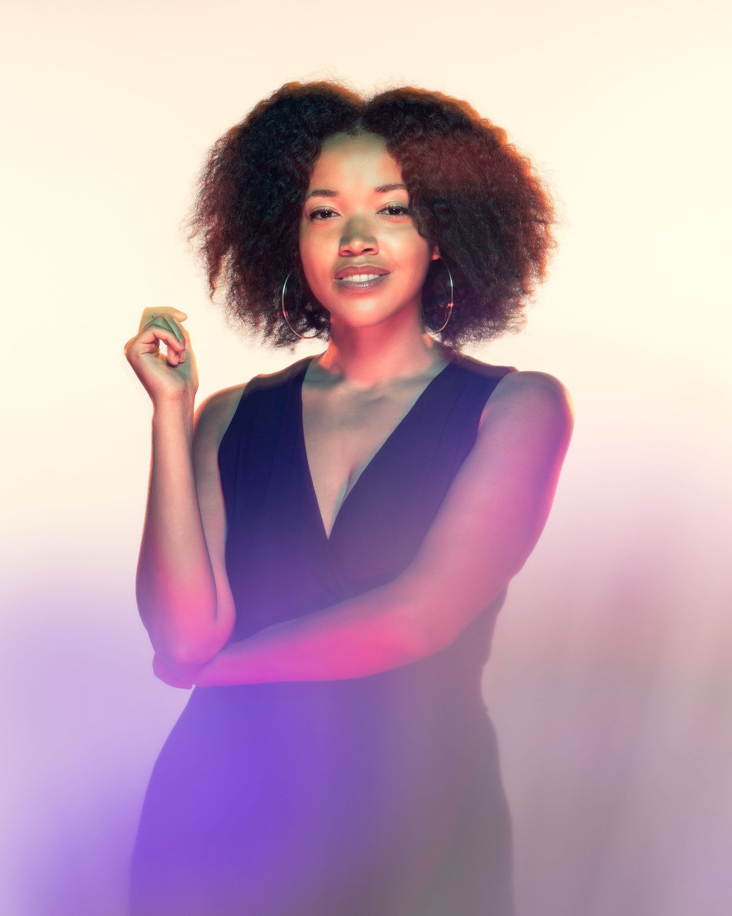 Portrait of a smiling woman with natural curly hair in soft purple neon studio lighting.