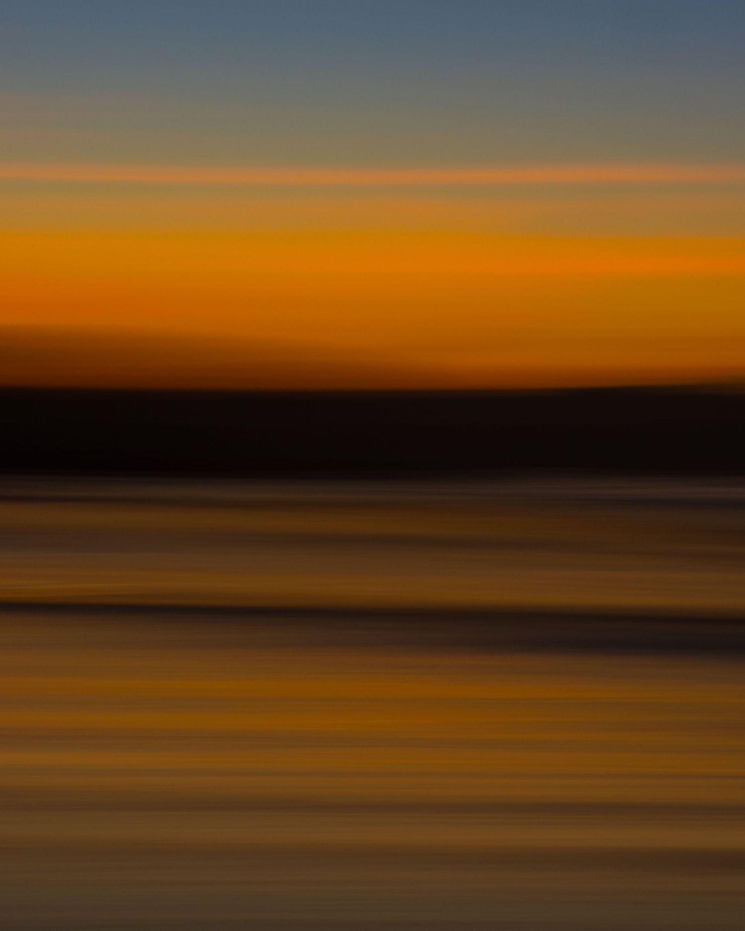 Abstract motion blur coastal sunset with warm golden tones and dark silhouetted shoreline.