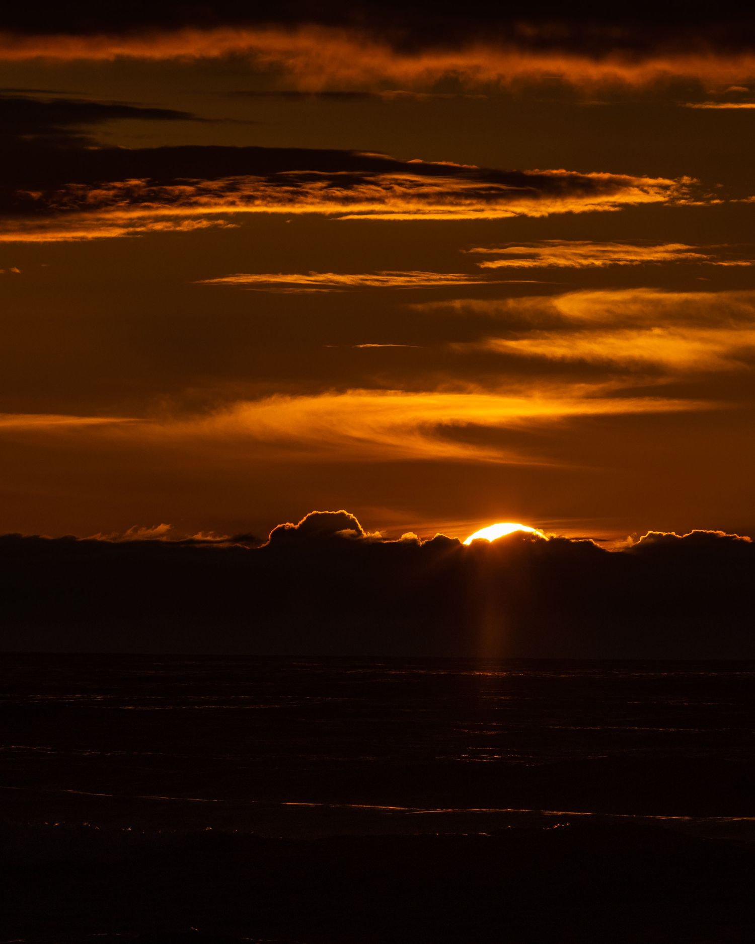 Fiery sunset with the sun breaking through dark clouds, casting golden rays over the ocean.