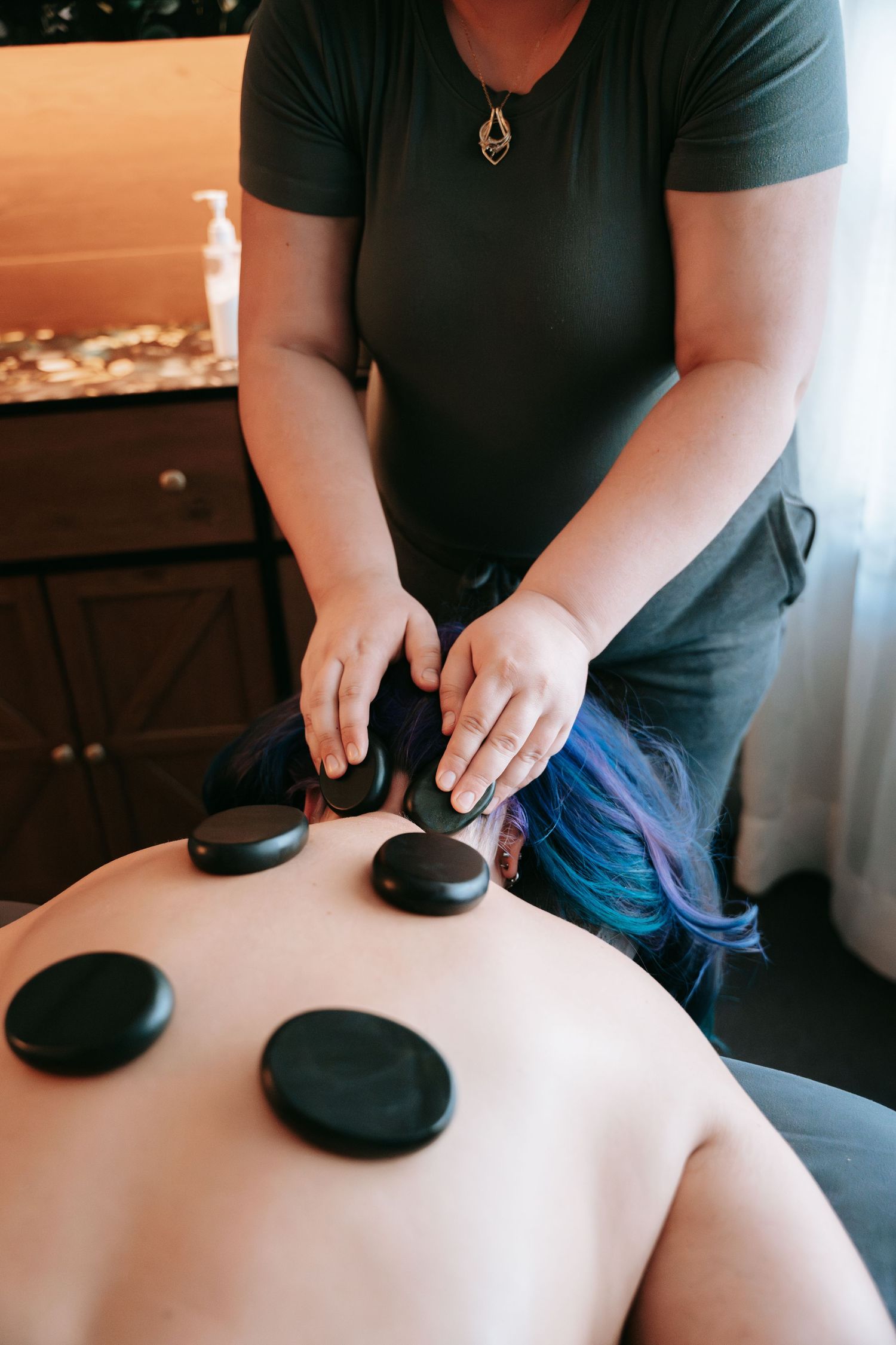 Massage therapist placing hot stones on clients back during professional hot stone massage therapy session.