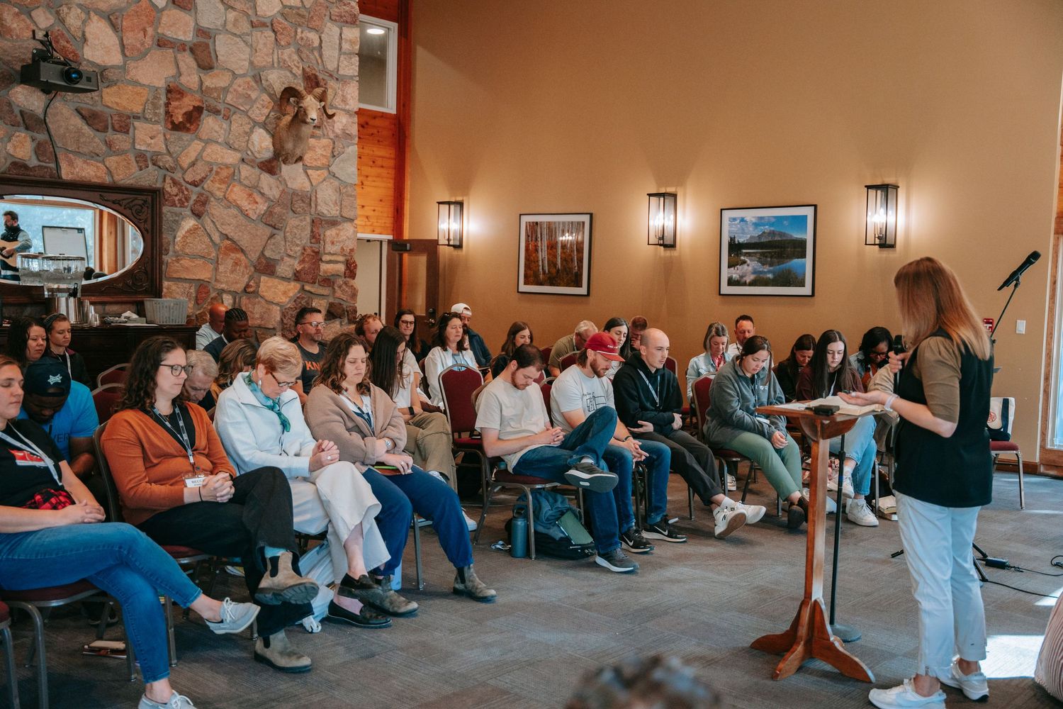 Speaker presenting to large engaged audience in rustic stone-walled conference room at indoor event.