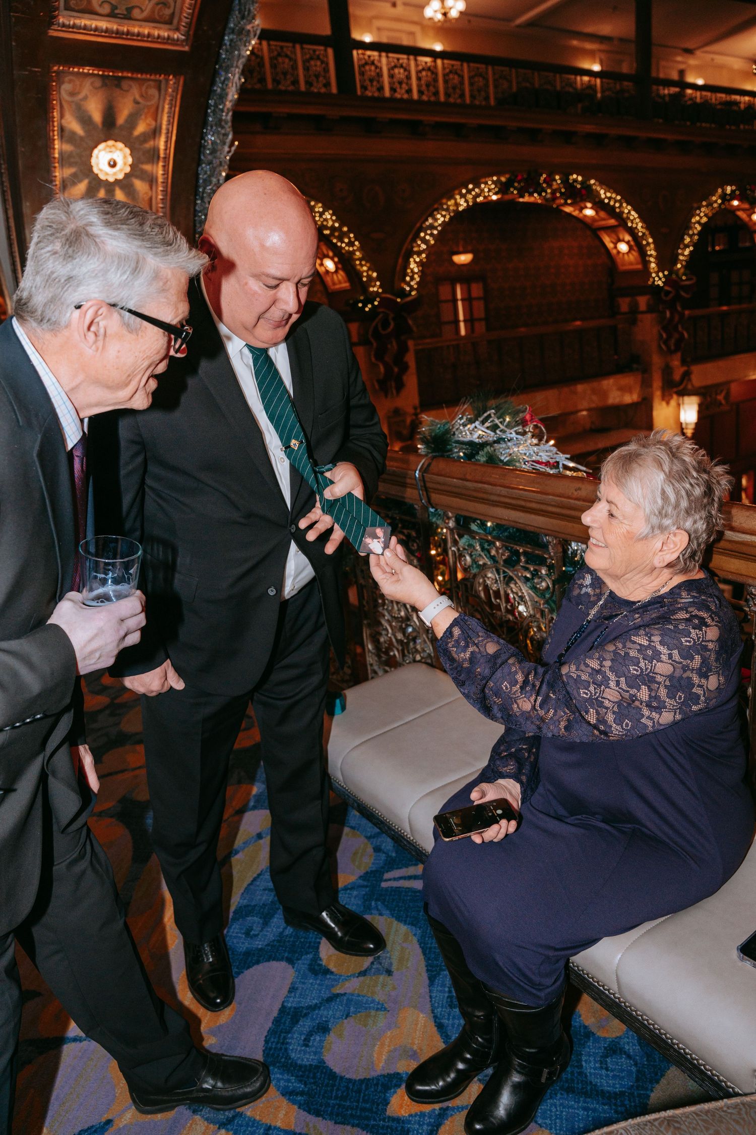 Three elegantly dressed wedding guests conversing in an ornate decorated venue interior.