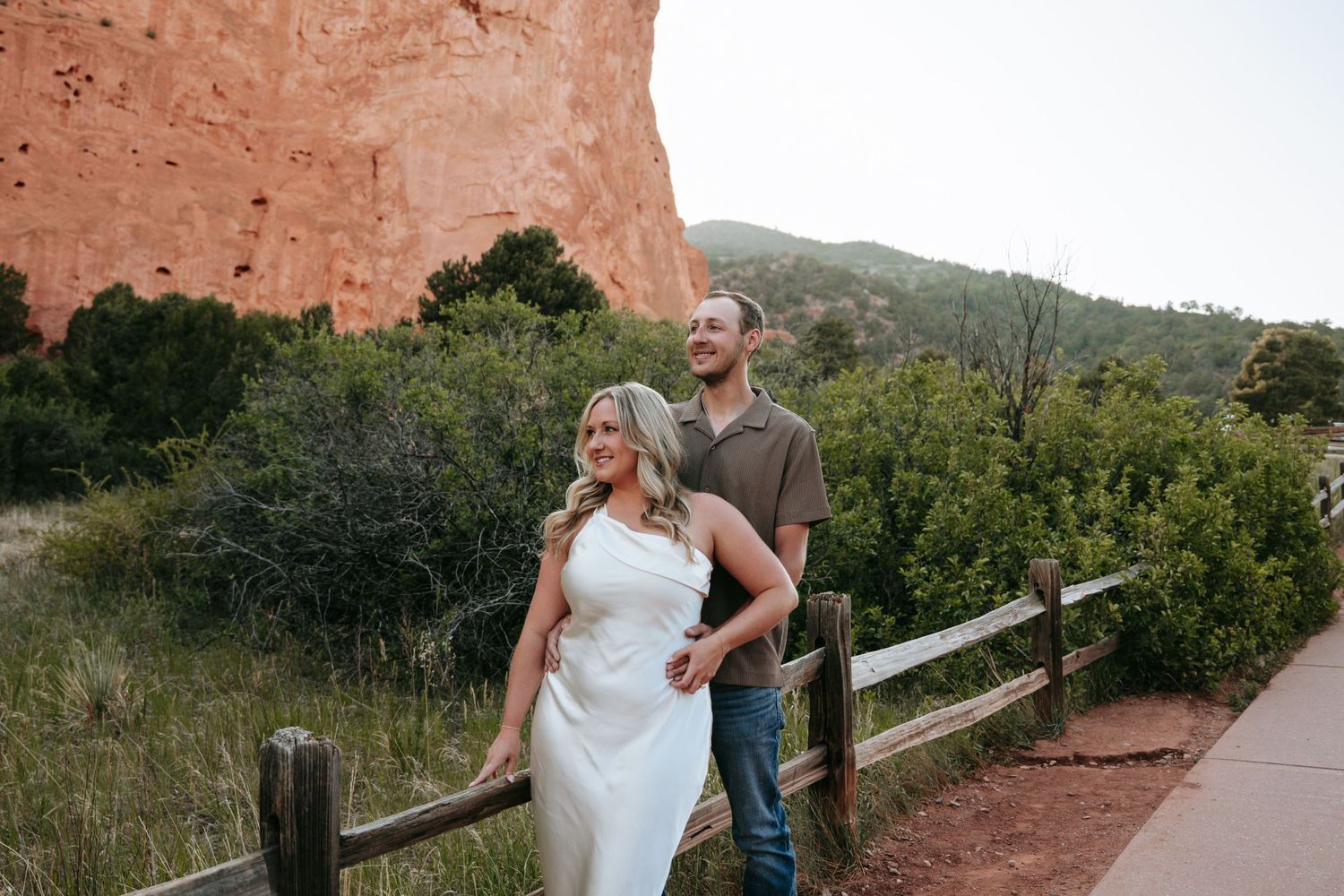 Couple posing by a wooden fence at Garden of the Gods, Colorado, with red rock formations in the background.