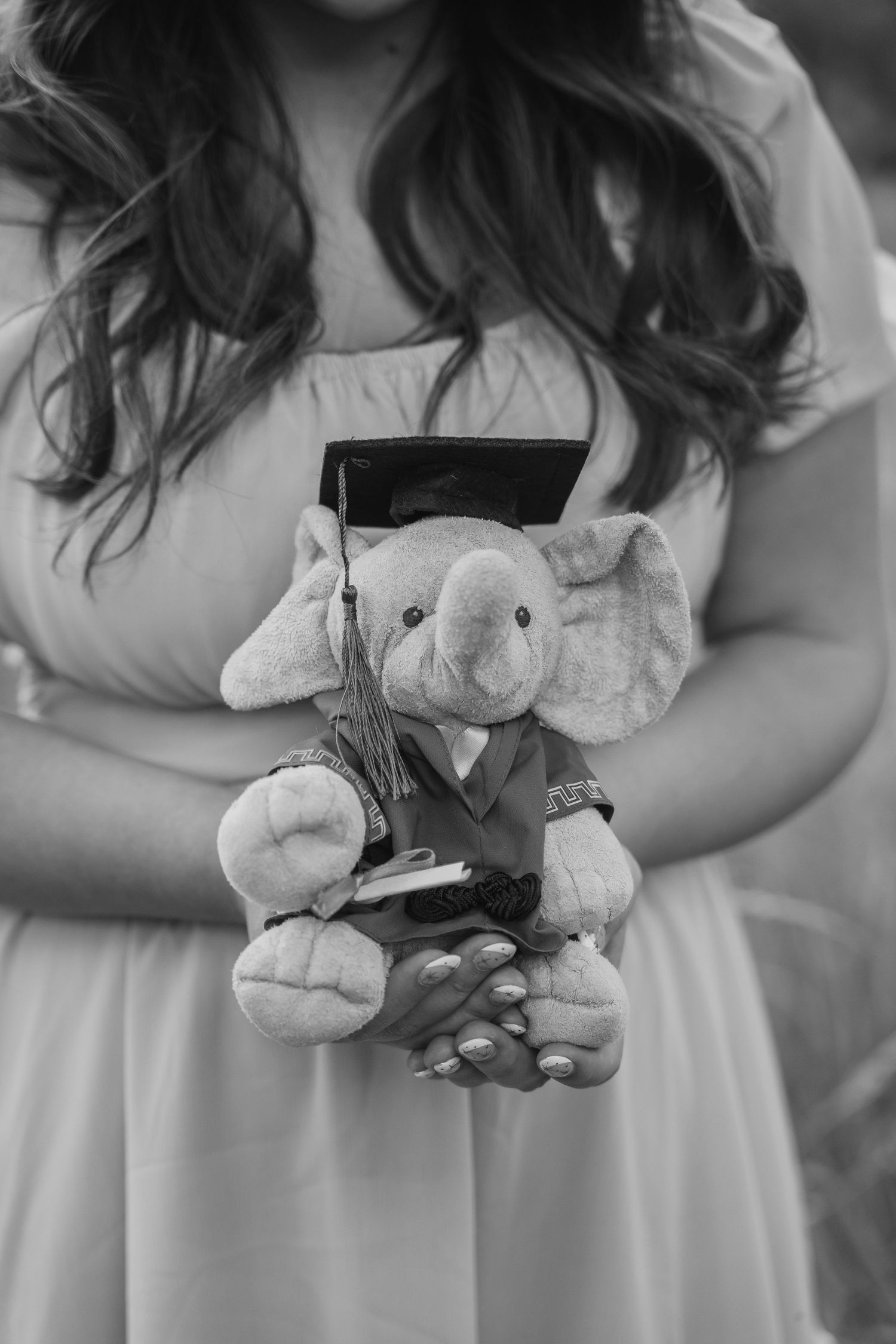 Black and white photo of a girl holding a graduation elephant stuffed animal wearing a cap and gown.