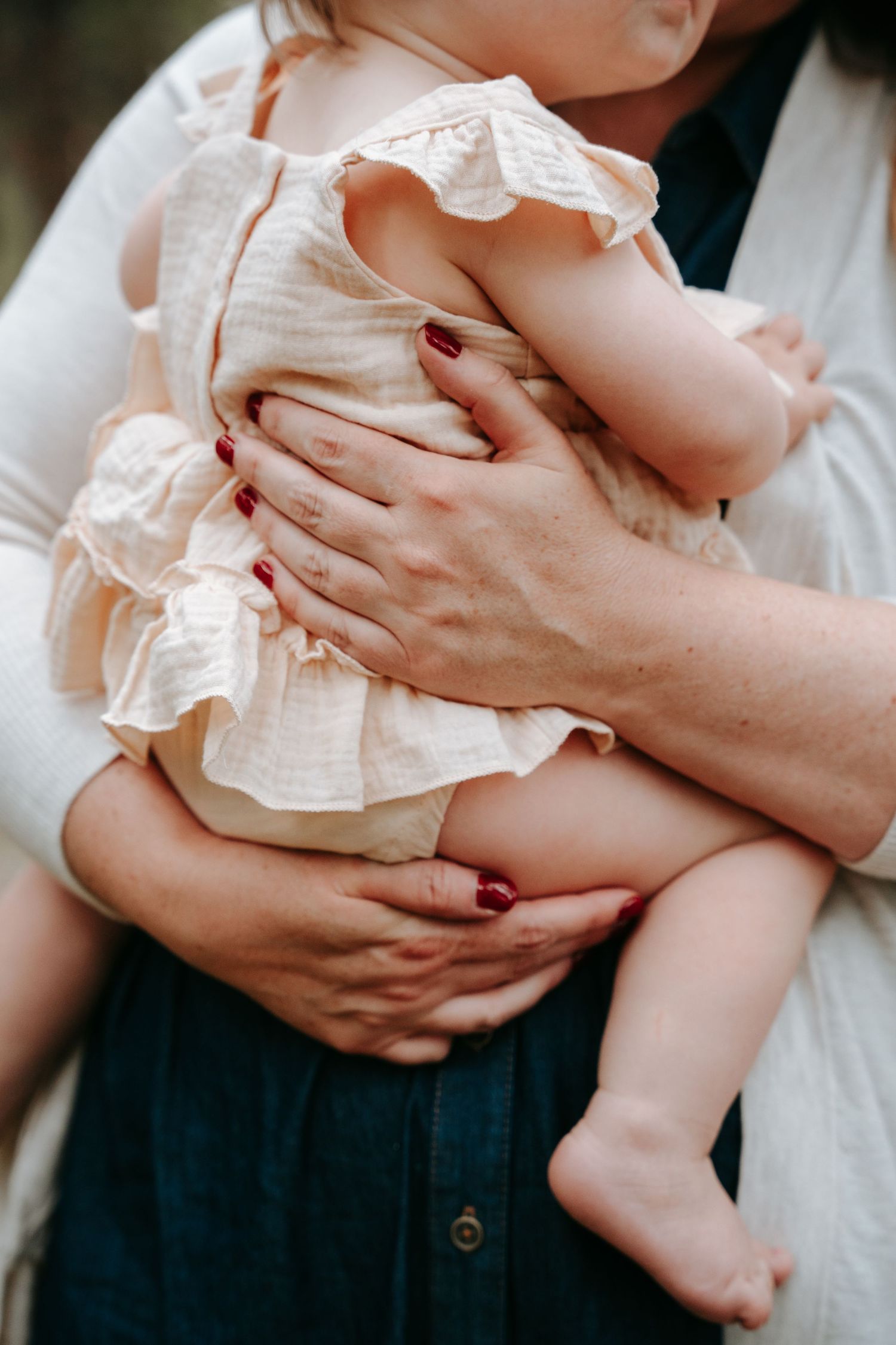 Mother holding a baby dressed in a cream ruffle outfit during an outdoor family photo session.