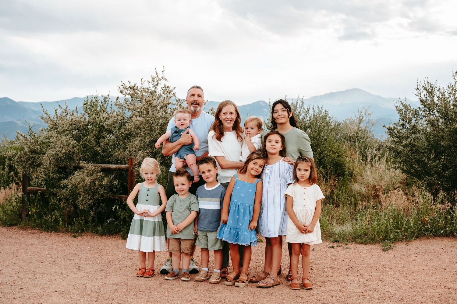 Family of ten with parents and eight children posing on a dirt path with mountains behind.
