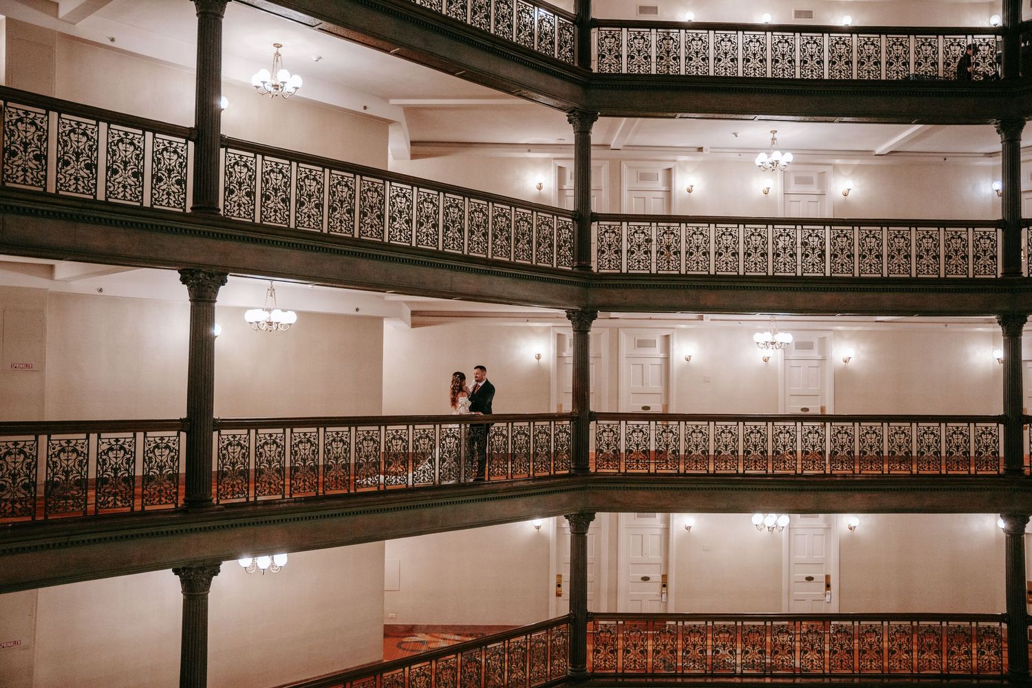 Couple shares romantic moment on ornate multi-level balcony with decorative iron railings.