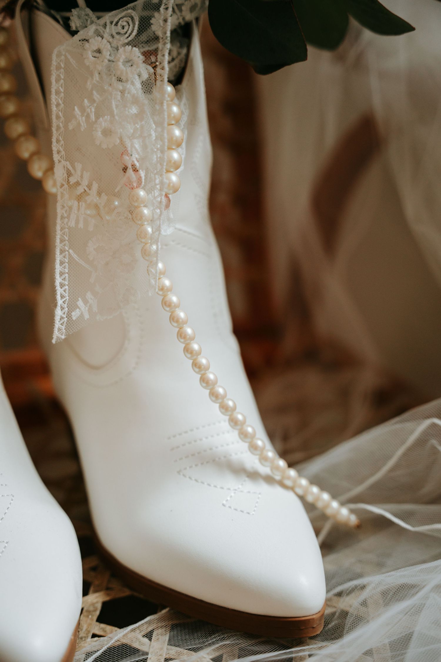 White bridal cowboy boot adorned with lace and pearl necklace draped elegantly for a rustic wedding.