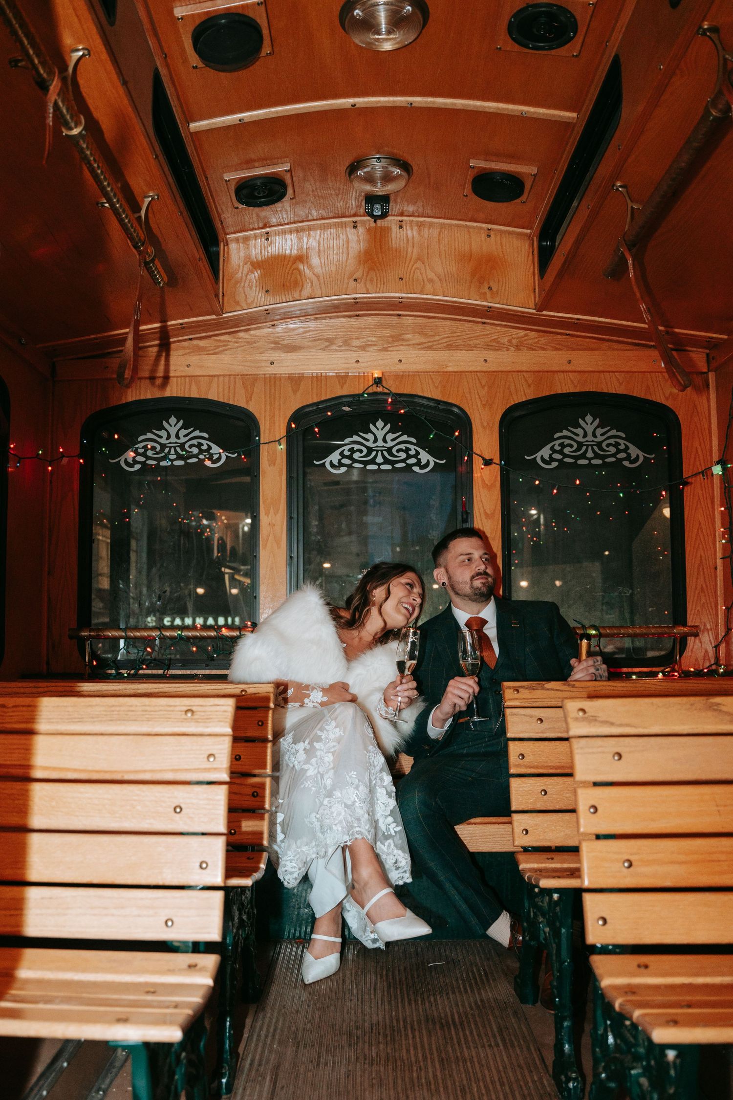Bride and groom laugh together holding champagne glasses inside a vintage wooden trolley car.