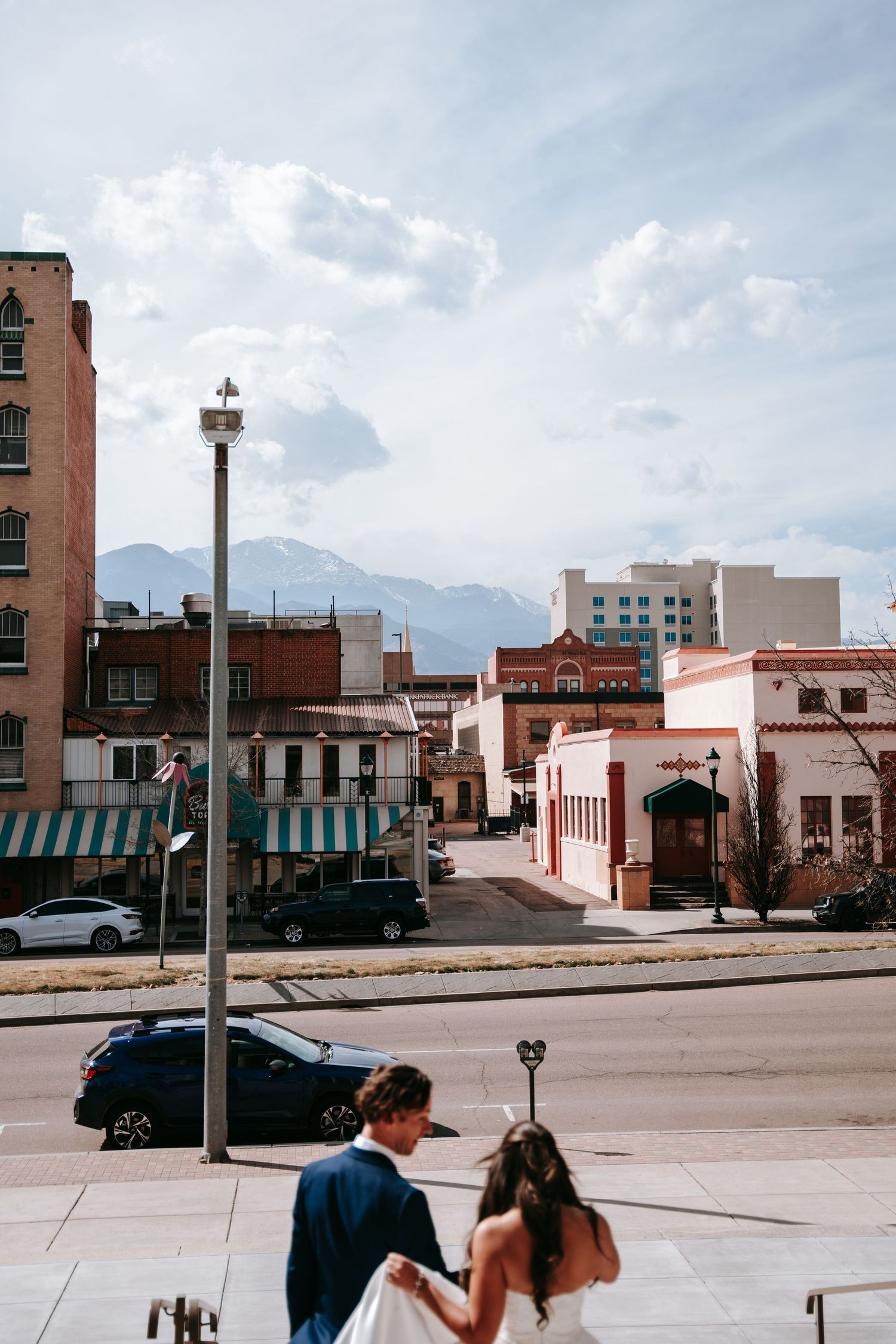 Wedding couple walking hand in hand through downtown street with mountain views.