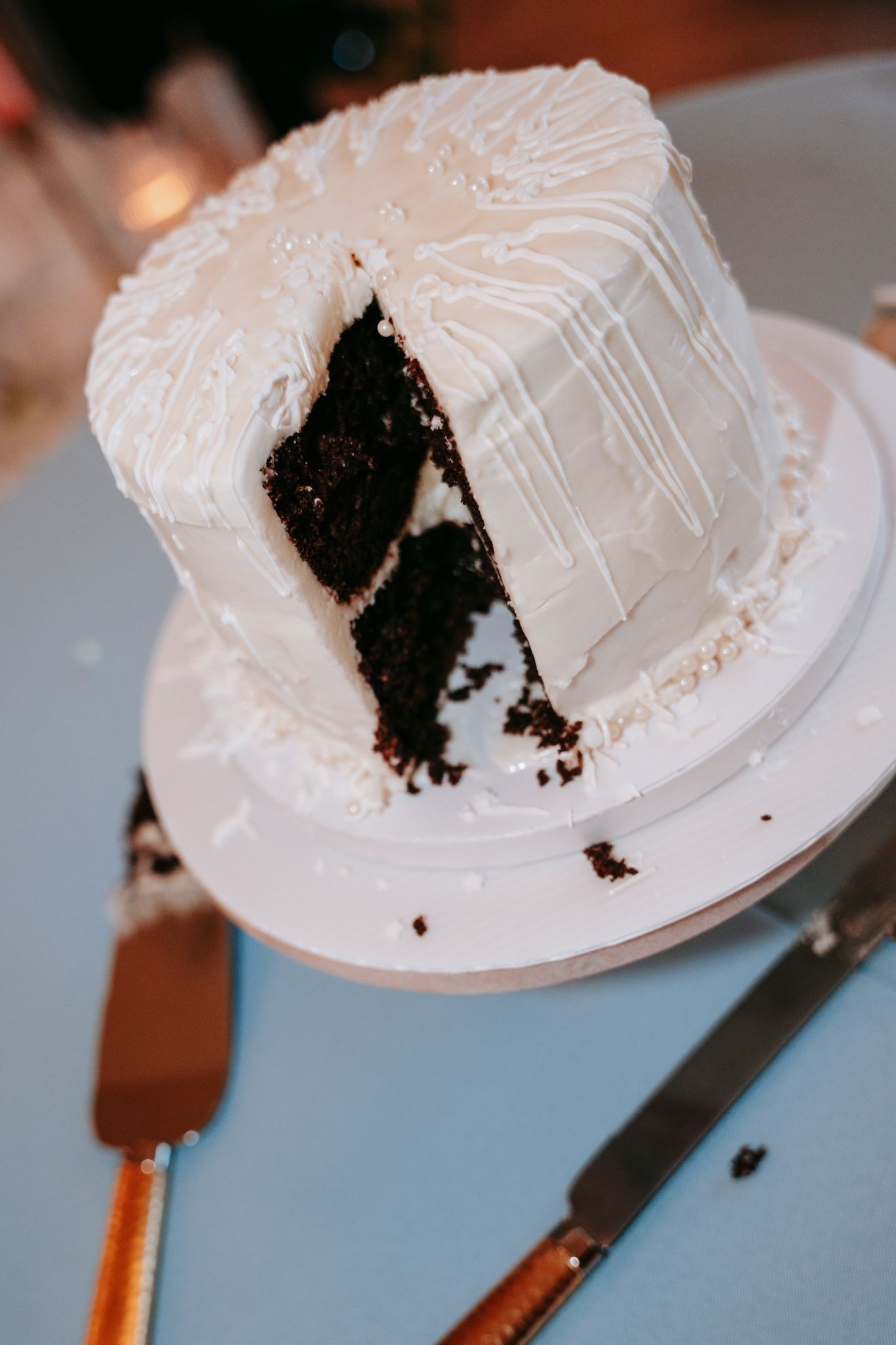White frosted chocolate wedding cake with a slice removed revealing dark layers on a cake stand.
