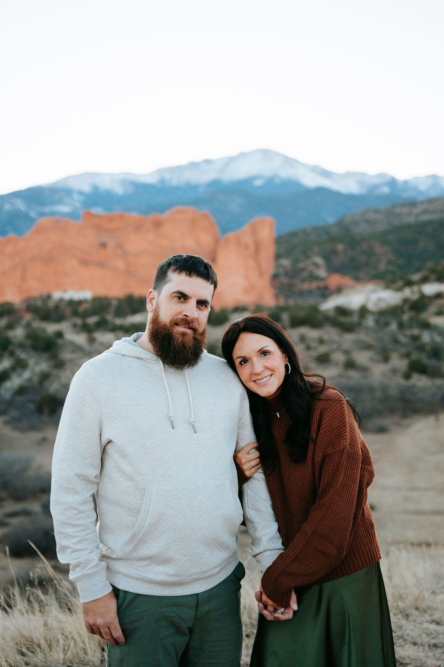 Bearded man in hoodie and woman in brown sweater posing at Garden of the Gods.