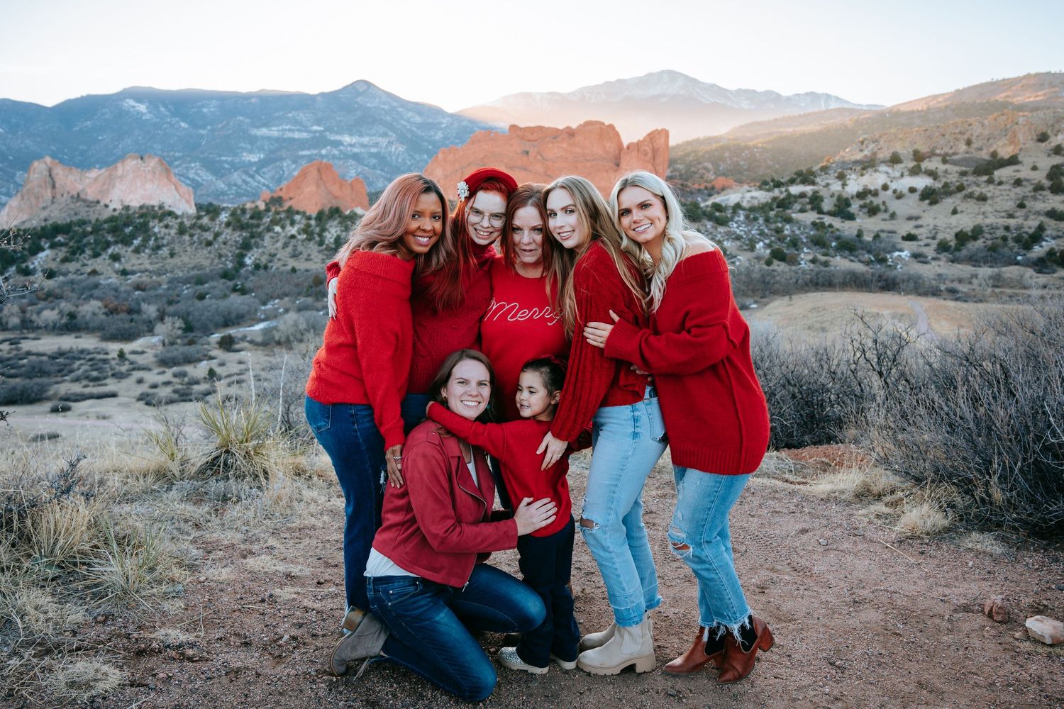 Group of seven women in matching red sweaters posing at Garden of the Gods Colorado landmark.