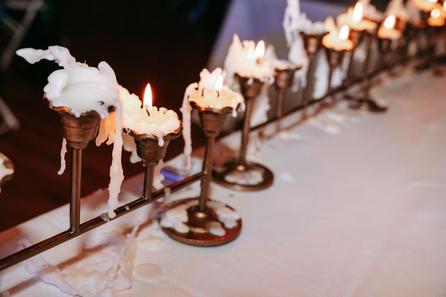 Row of dripping white candles on brass candlesticks illuminate a romantic wedding reception table.