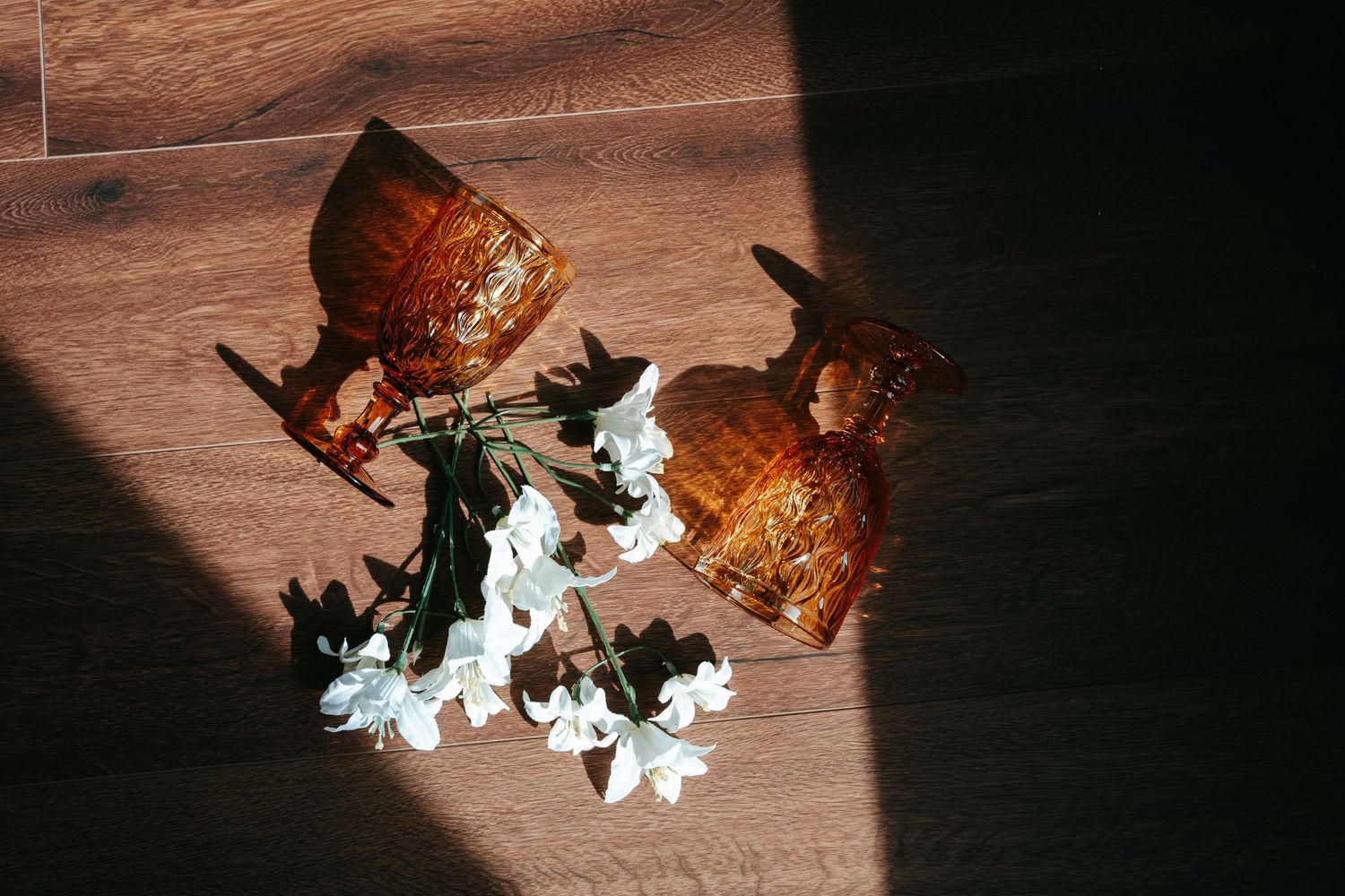 Two amber glass vases with white flowers casting shadows on hardwood floor.