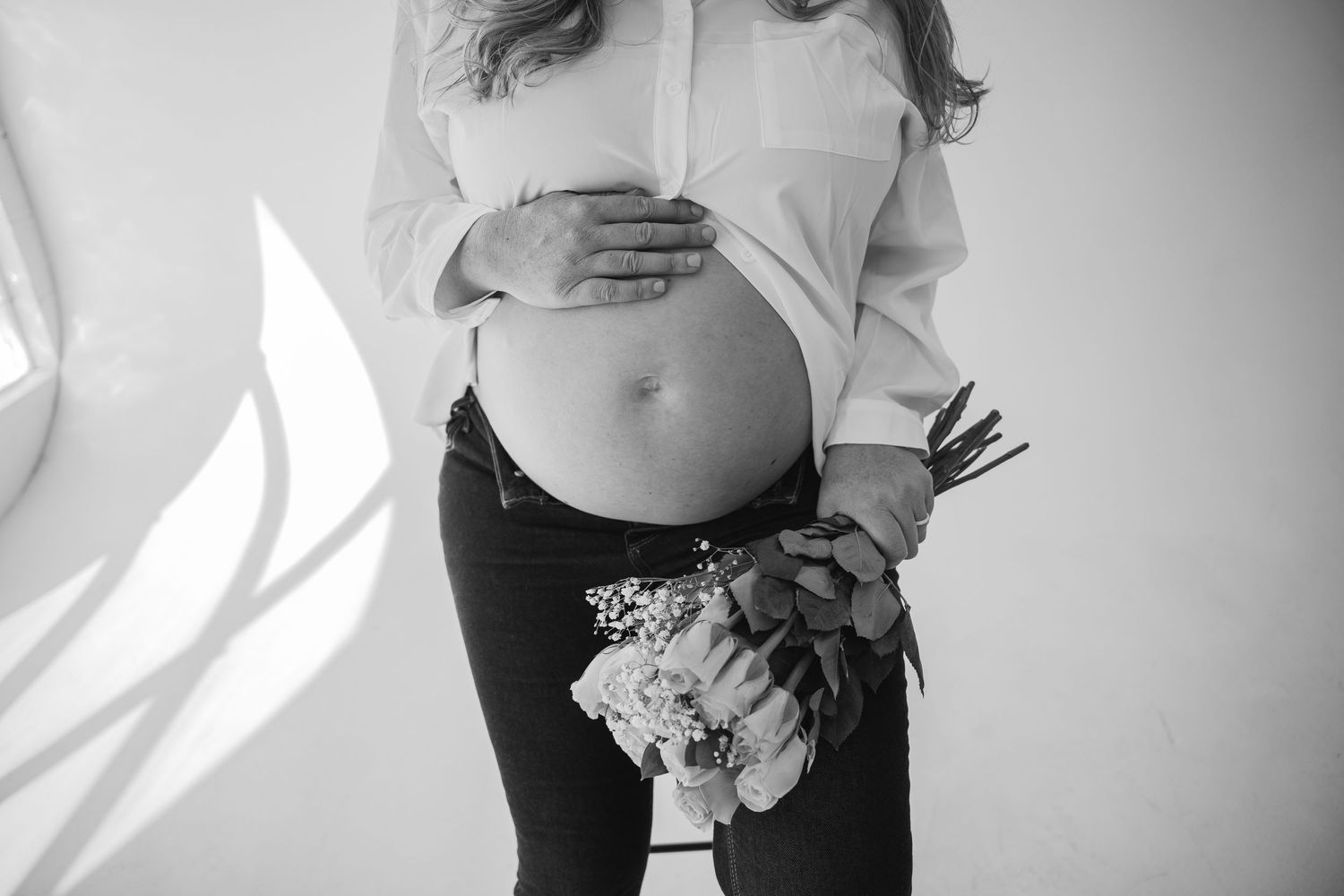 Black and white photo of pregnant woman cradling belly while holding a small bouquet of flowers.