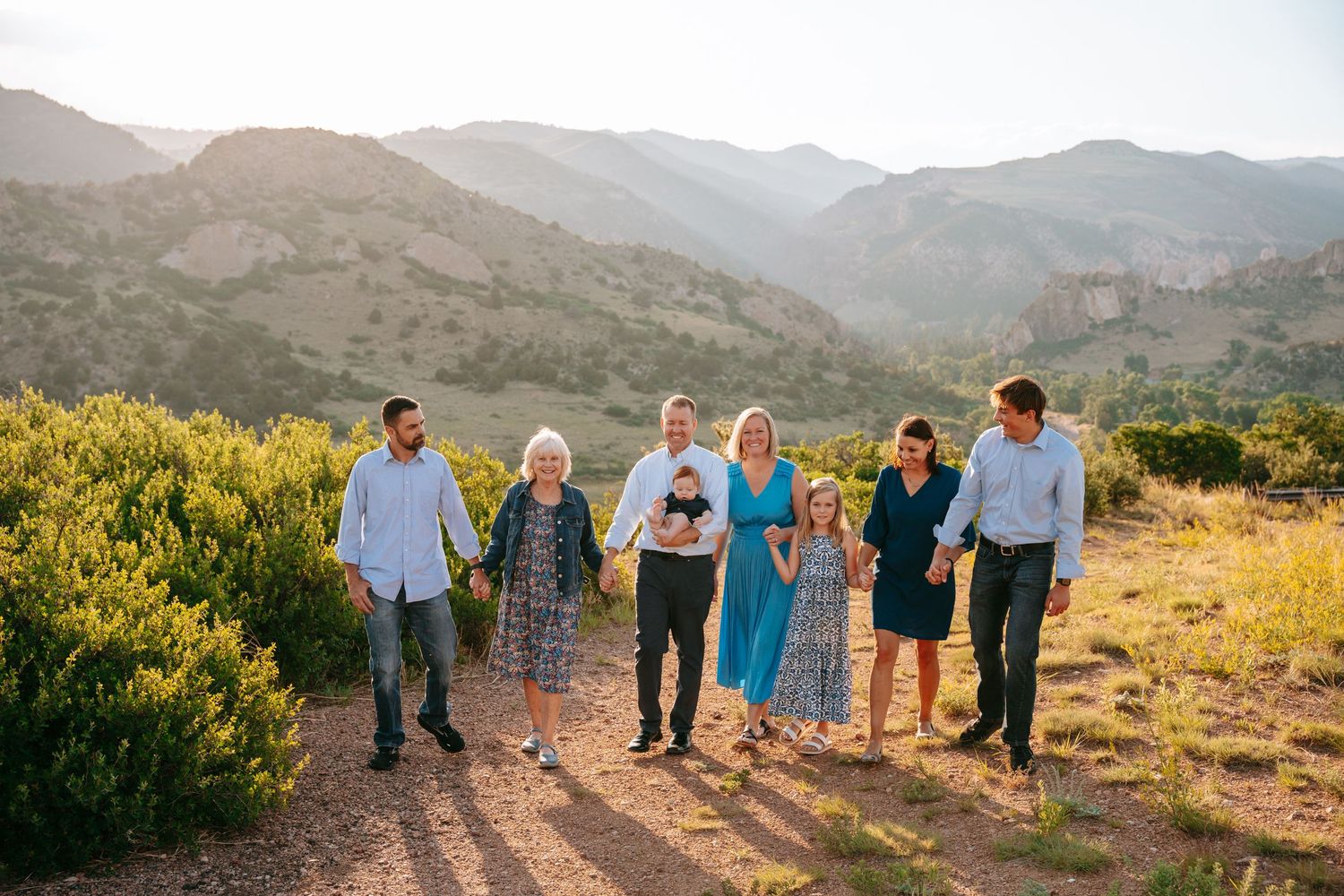 Multi-generational family walking together on a sunny mountain trail path.