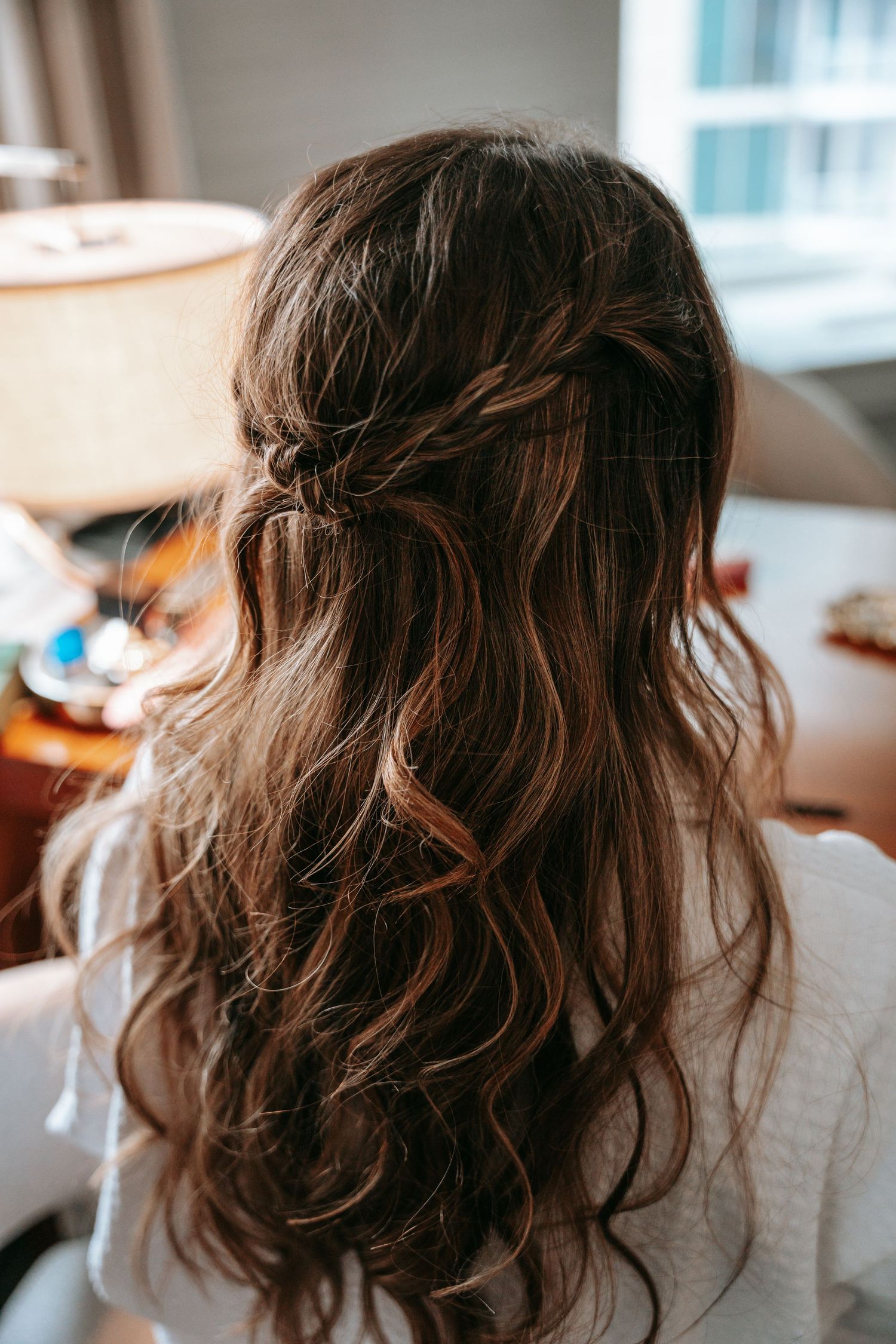 Bride's elegant half-up twisted hairstyle with long wavy brown hair viewed from behind.