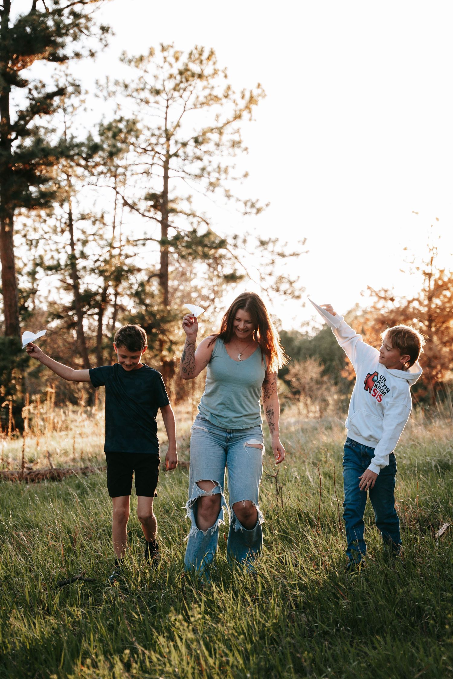 Mother and two sons walk and dance together through a sunlit meadow during a warm outdoor family session.
