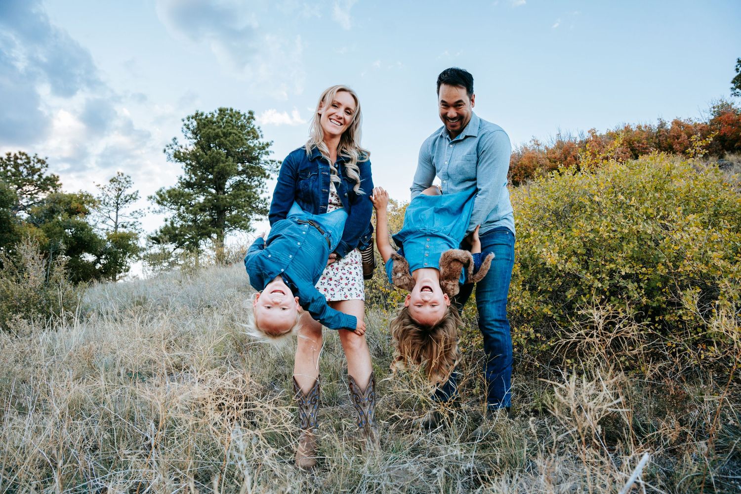 Parents playfully holding two children upside down in a grassy Colorado hillside meadow.