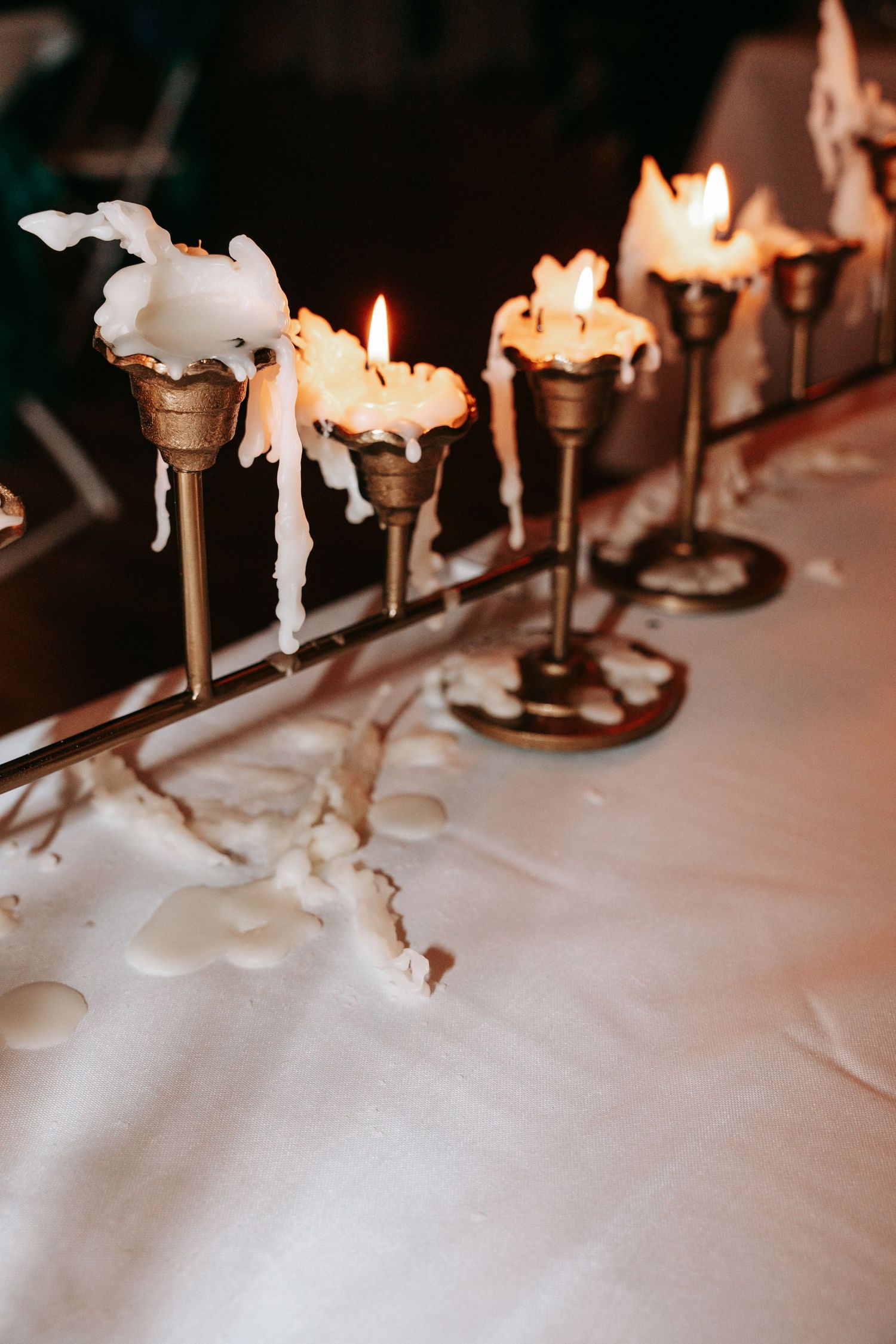 Elegant brass candelabras with melting white candles dripping wax on a white linen table.