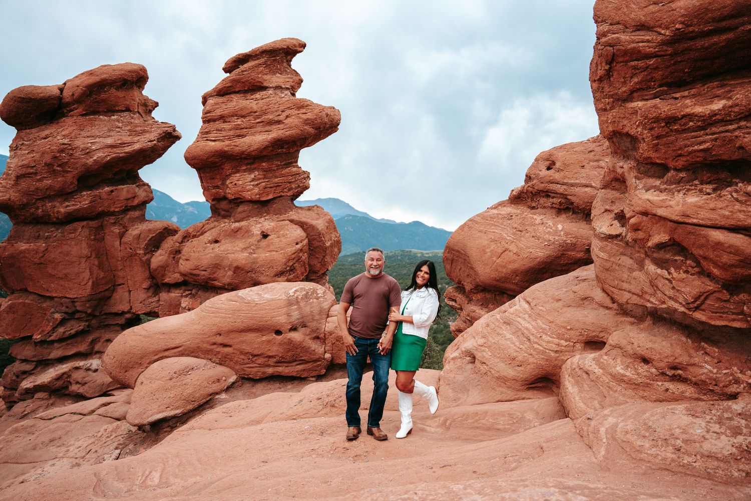 Smiling couple posing between iconic red rock formations at Garden of the Gods in Colorado.