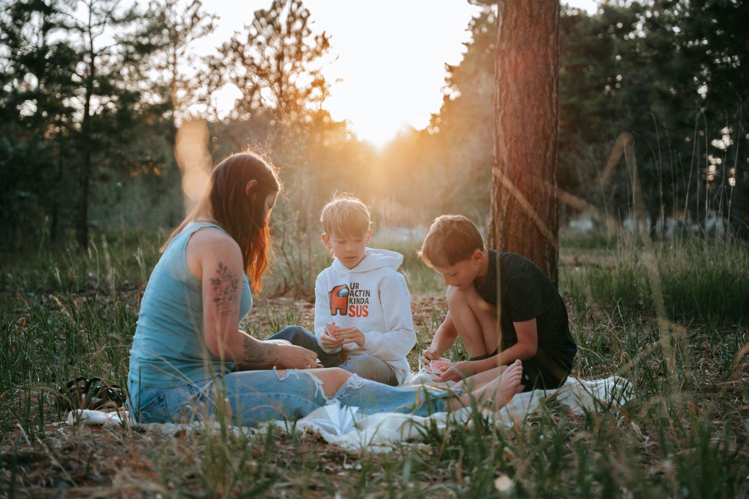 Family enjoying a golden hour picnic in a forest clearing, sitting together on a blanket among trees.