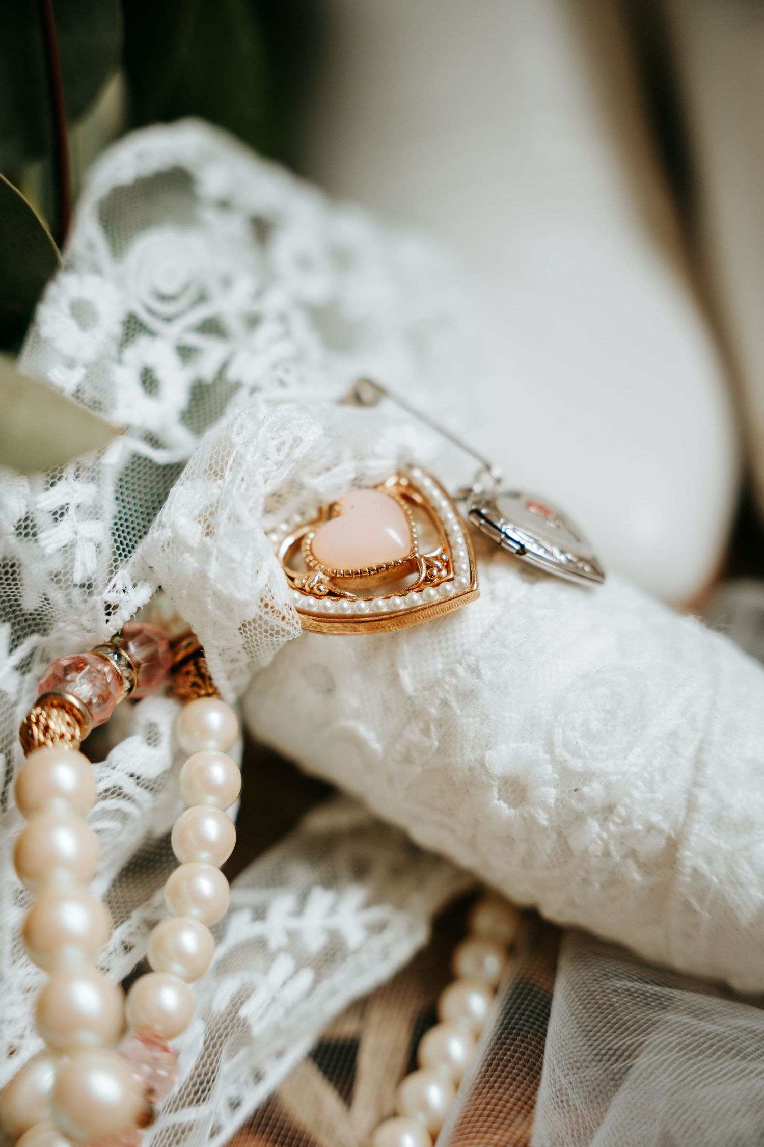 Heart-shaped gold locket and pearl bracelet resting on white lace bridal boot detail.