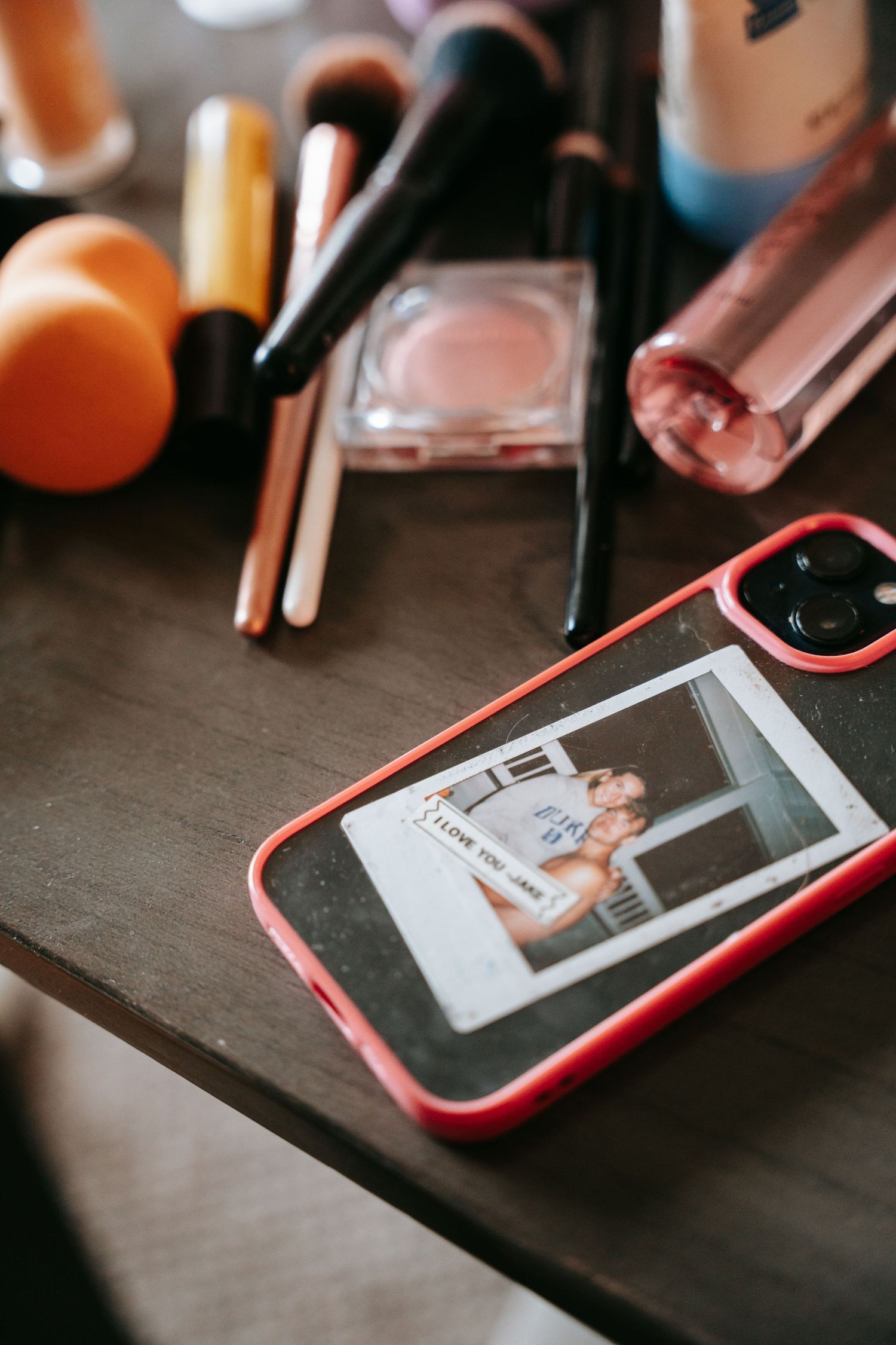 Phone with couples Polaroid photo on makeup vanity surrounded by brushes and beauty products.